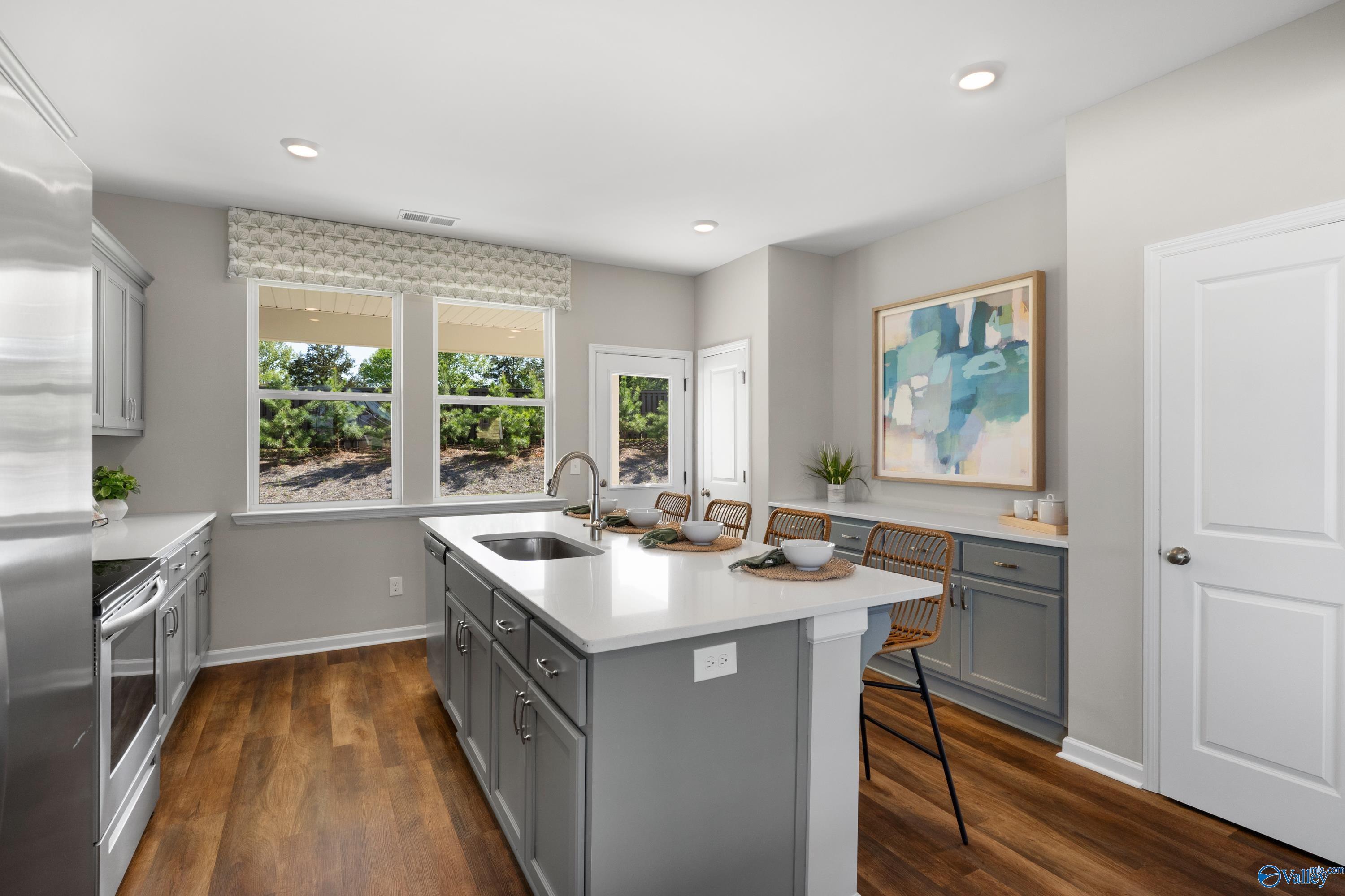 Modern kitchen featuring white shaker cabinets, gray island with quartz counters, stainless appliances, and wooded backyard view in The Stella floor plan, Madison, AL