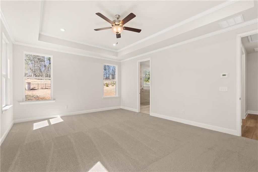 Spacious bedroom with tray ceiling, ceiling fan, beige carpet, and en-suite bath in Davidson Homes Danbury C, Buford GA