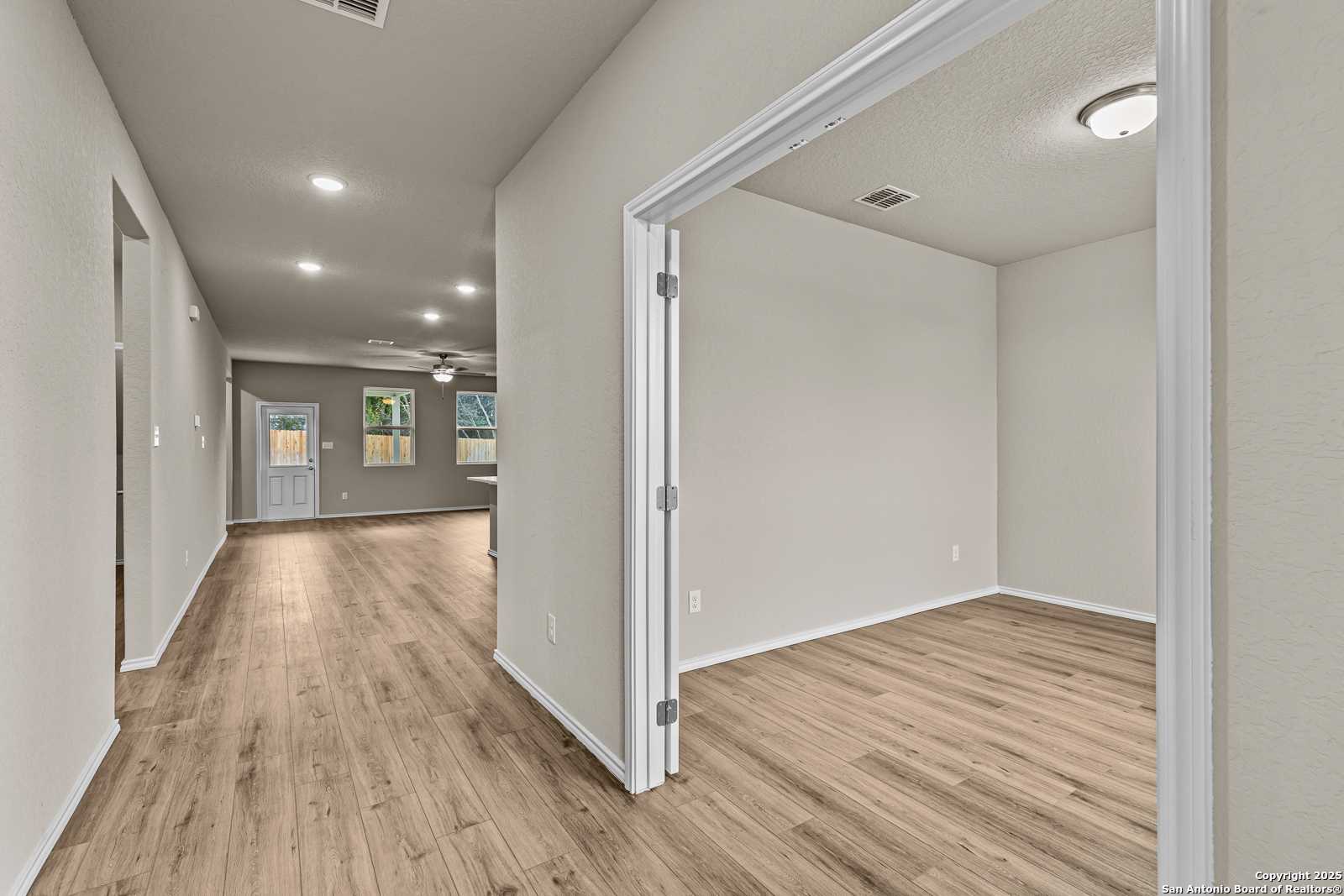 Spacious hallway with light hardwood floors, white walls, and open doorways in Davidson Homes The Douglas F, San Antonio