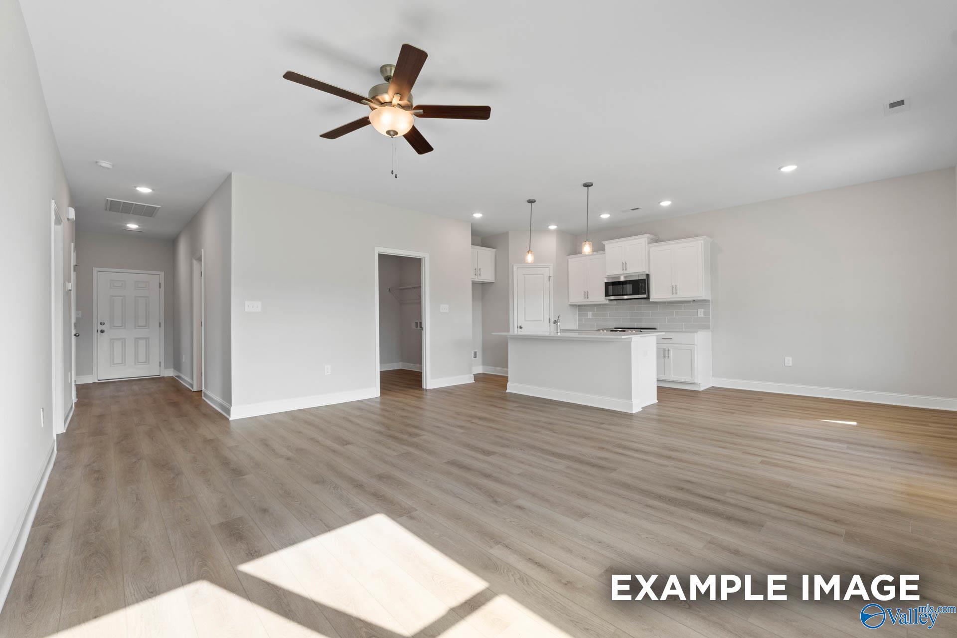 Open-concept living and kitchen with white cabinets, island, hardwood floors, and ceiling fan in Davidson Homes The Butler, New Market, Alabama