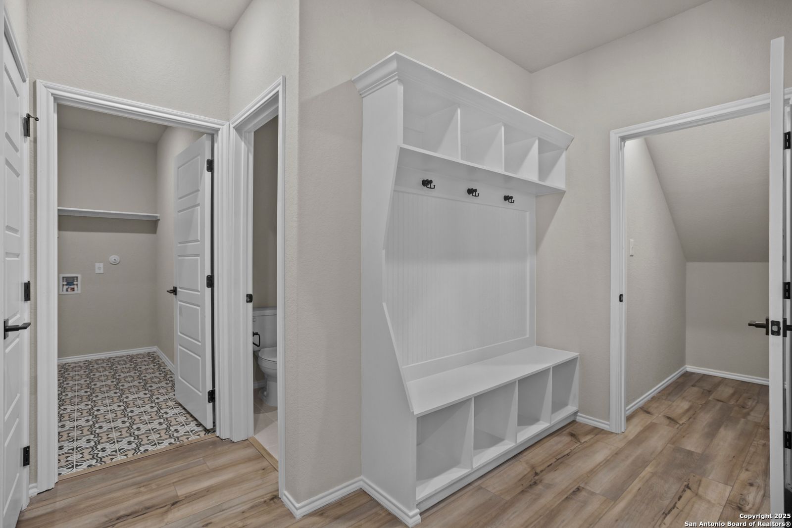 Functional mudroom with white built-in cabinet, hooks, bench, adjacent laundry room and half bath in Davidson Homes The Douglas F, Comanche Ridge, San Antonio