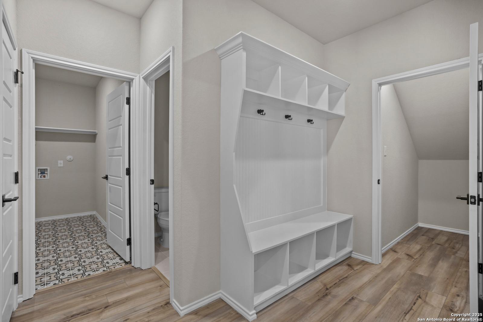 Functional mudroom with white built-in cabinet, hooks, bench, adjacent laundry room and half bath in Davidson Homes The Douglas F, Comanche Ridge, San Antonio