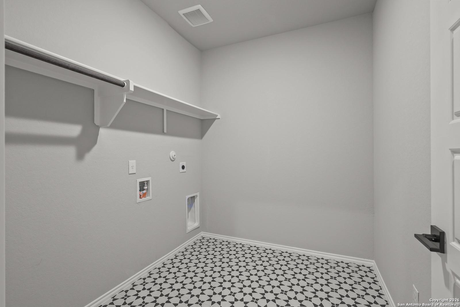 Modern laundry room with built-in shelves, washer/dryer hookups, pet door, and geometric tile floor in Davidson Homes The Murray K, San Antonio