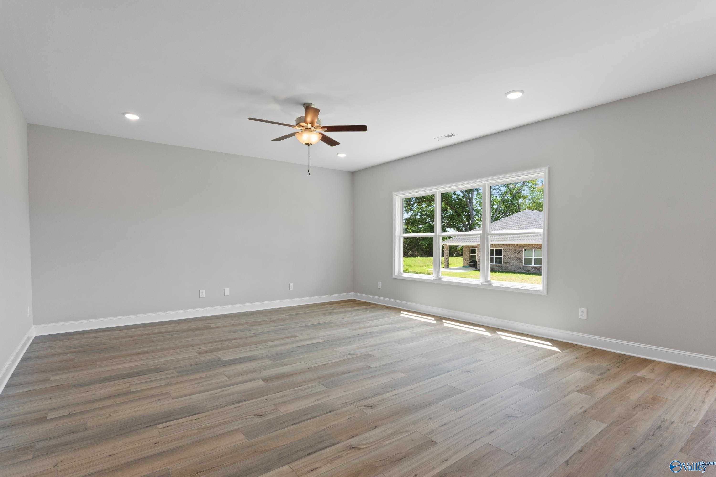 Bright empty bedroom with gray walls, hardwood floors, ceiling fan, and large window overlooking lawn in Davidson Homes The Chelsea B, New Market, AL