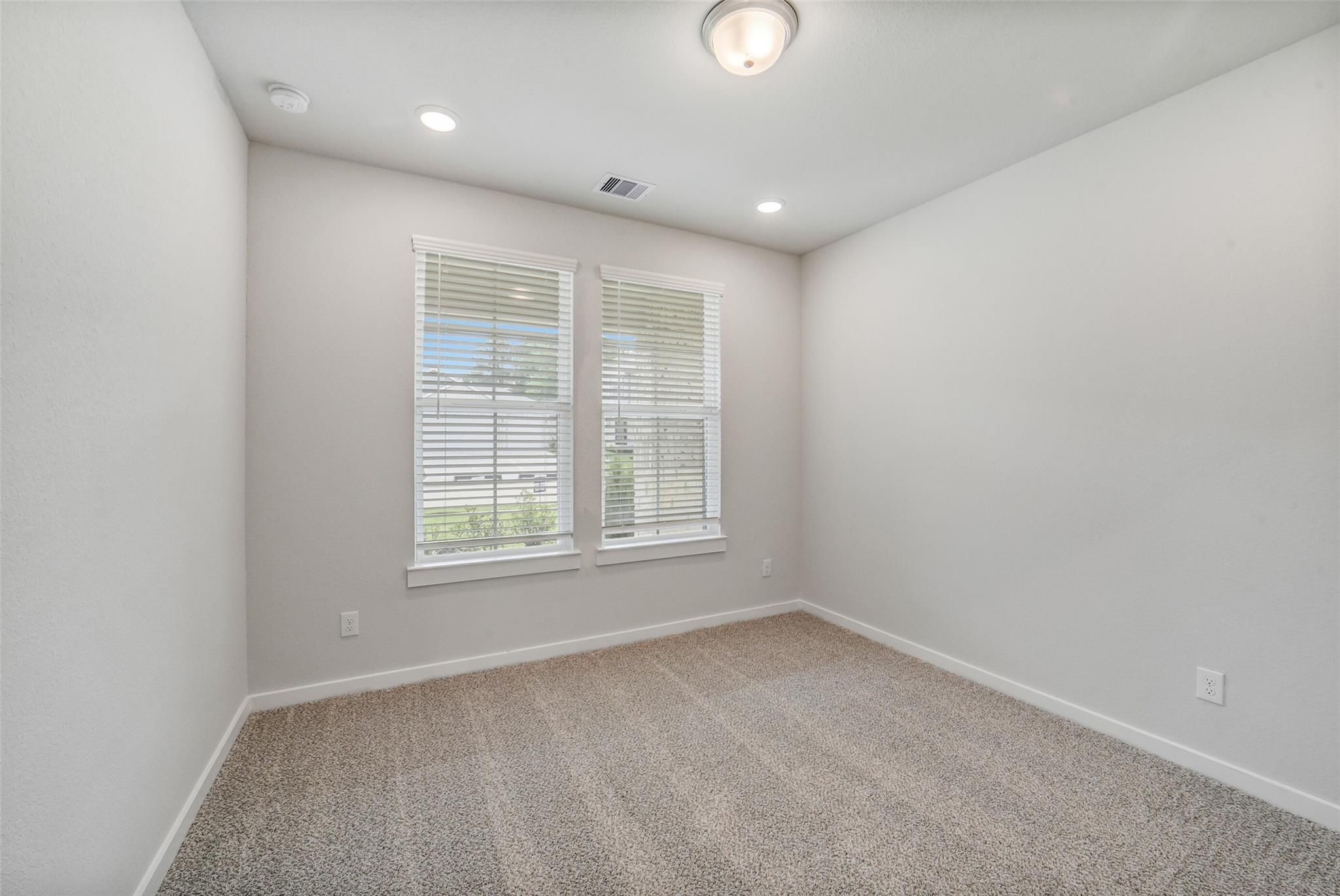 Empty bedroom with beige walls, tan carpet, double windows with blinds in Davidson Homes The Acadia C, Magnolia Texas