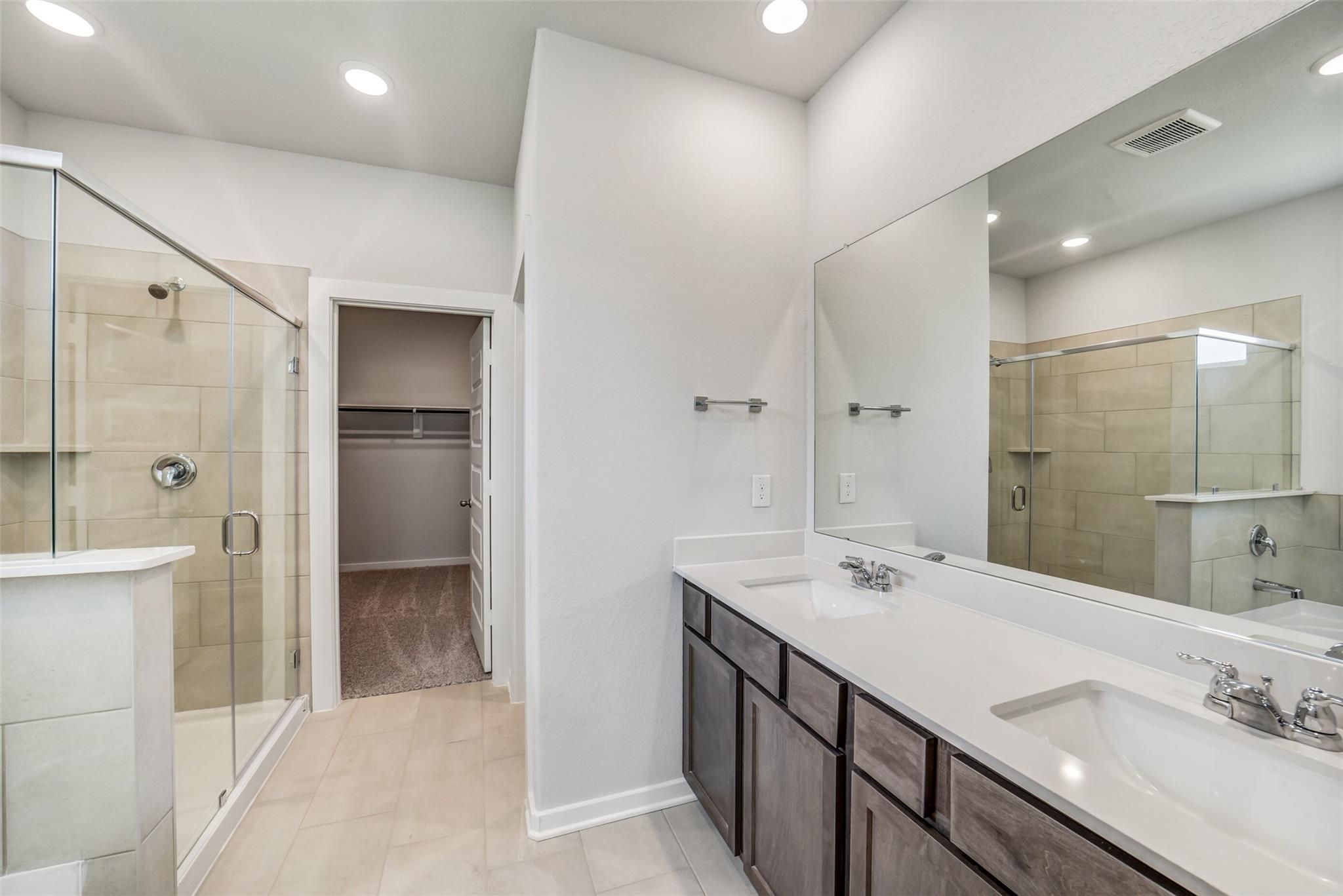 Modern master bathroom with frameless glass shower, double quartz vanity, dark cabinets in Davidson Homes The Acadia C, Magnolia TX