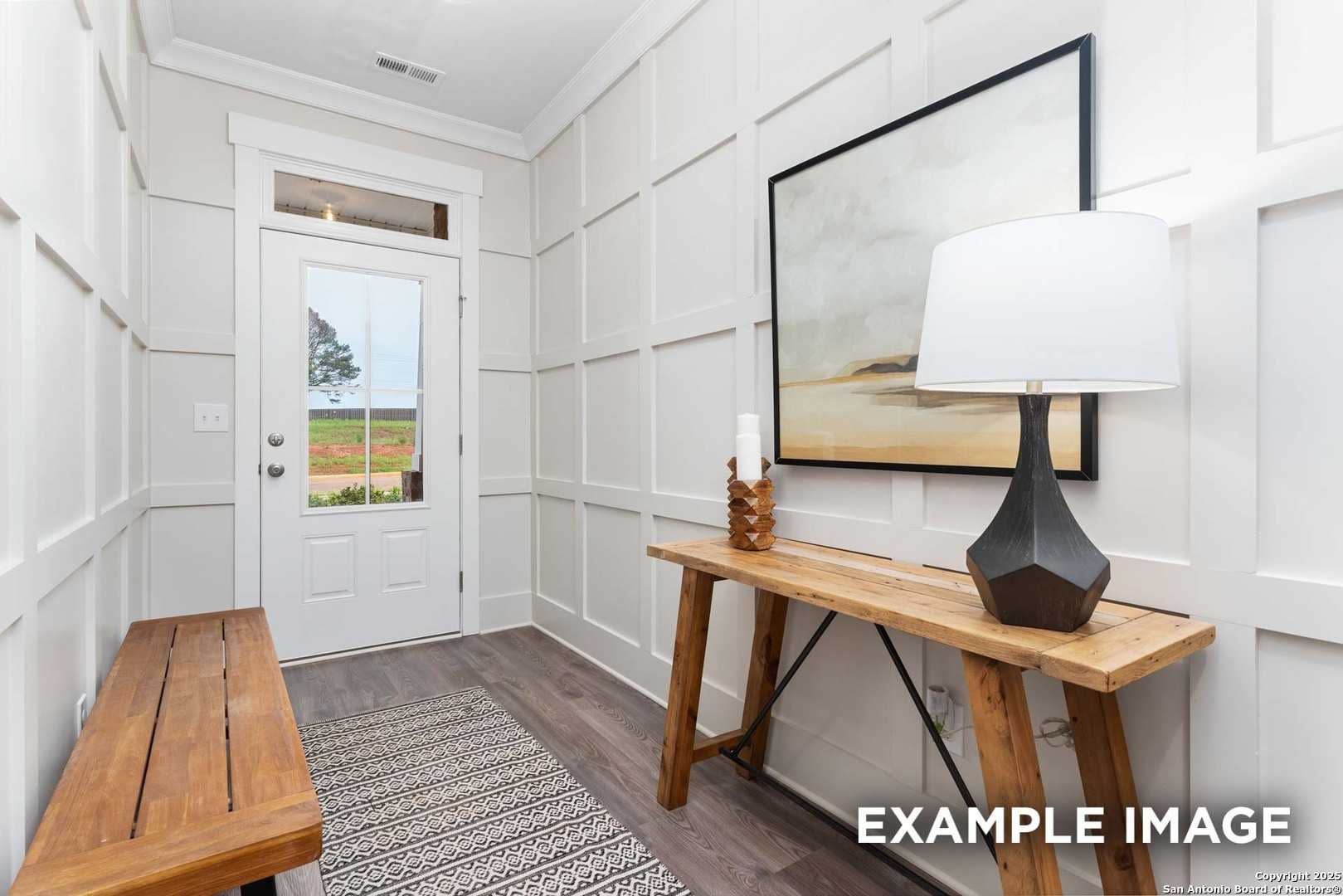 Bright entryway with white shiplap walls, wooden bench, console table lamp, abstract art, and glass door to field view in Davidson Homes The Daphne H, Seguin, Texas