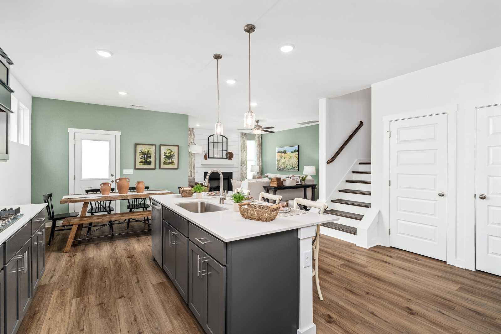 Spacious open-concept kitchen at Calista Farms in White House TN with gray cabinets, white island sink, pendant lights, hardwood floors
