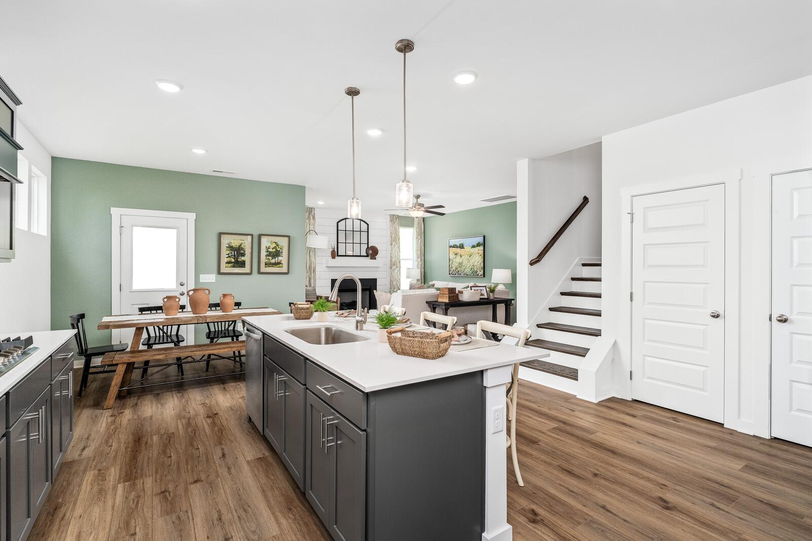 Spacious open-concept kitchen at Calista Farms in White House TN with gray cabinets, white island sink, pendant lights, hardwood floors