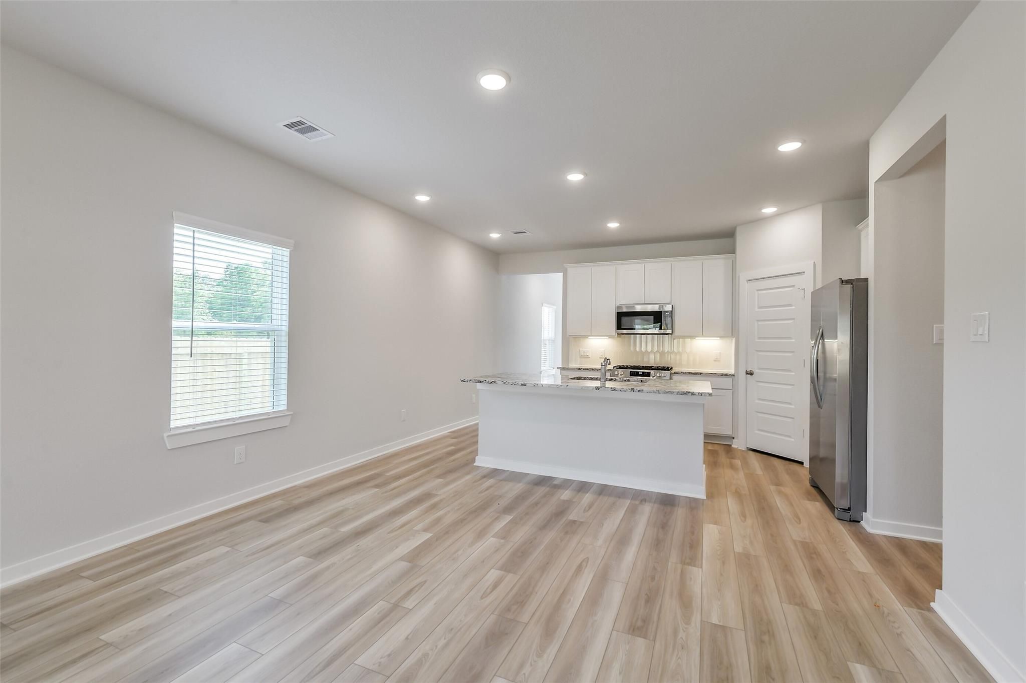 Modern open-concept kitchen featuring white cabinets, granite island, stainless appliances, and luxury vinyl plank floors in The San Marcos E, Conroe, TX