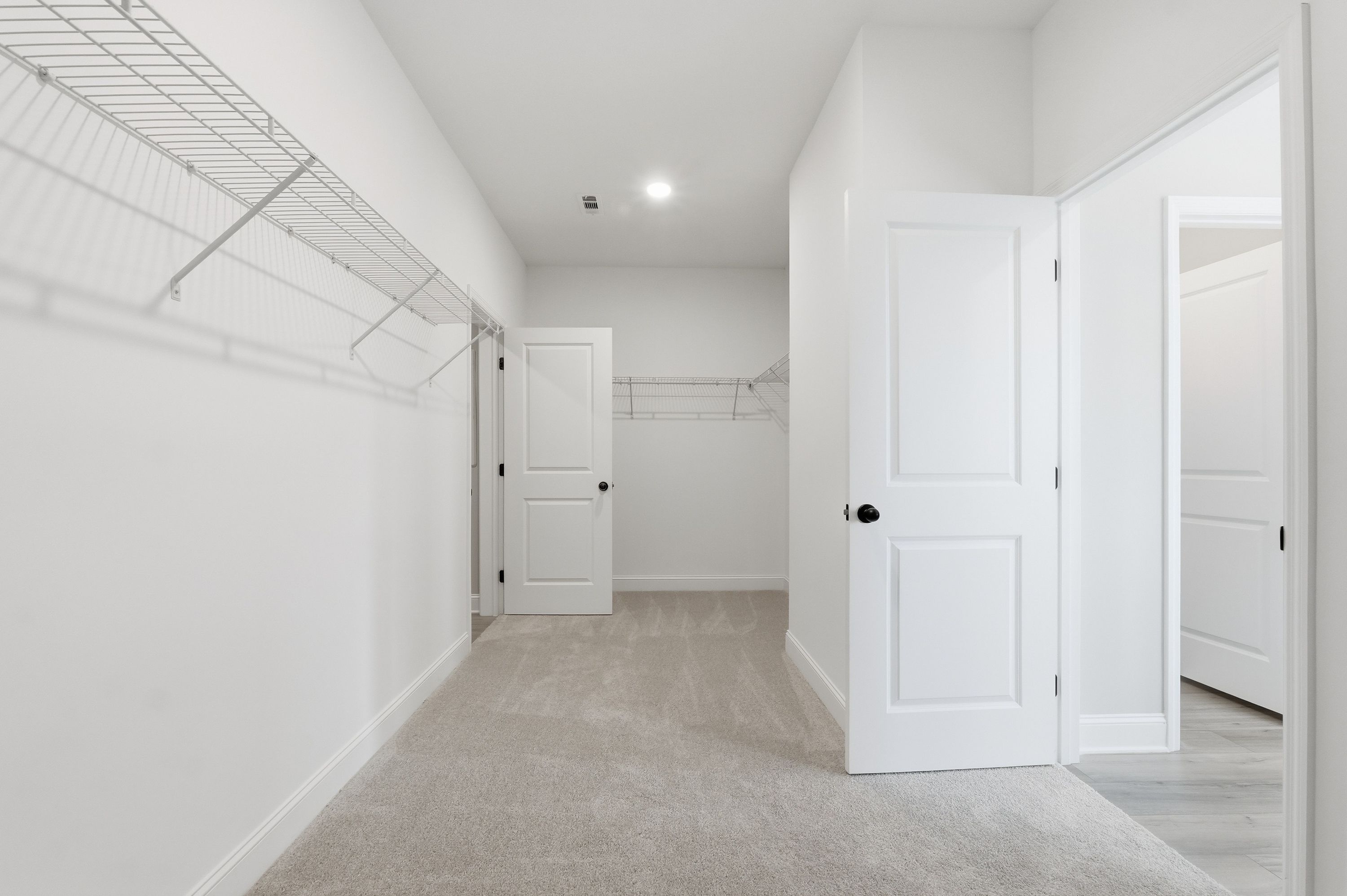 Spacious walk-in closet in The Rockford master suite featuring wire shelving, white doors, and neutral carpet flooring