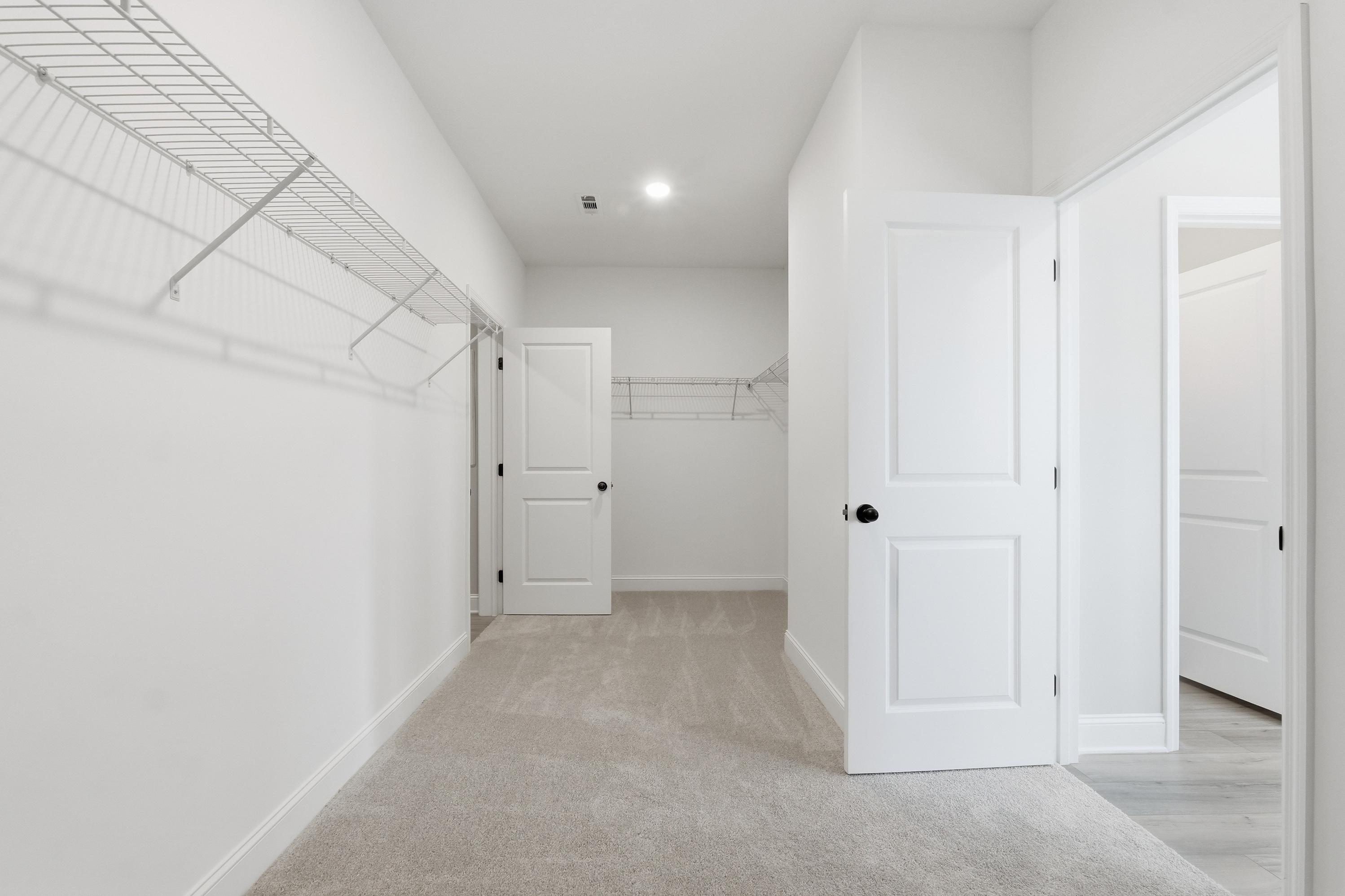 Spacious walk-in closet in The Rockford master suite featuring wire shelving, white doors, and neutral carpet flooring