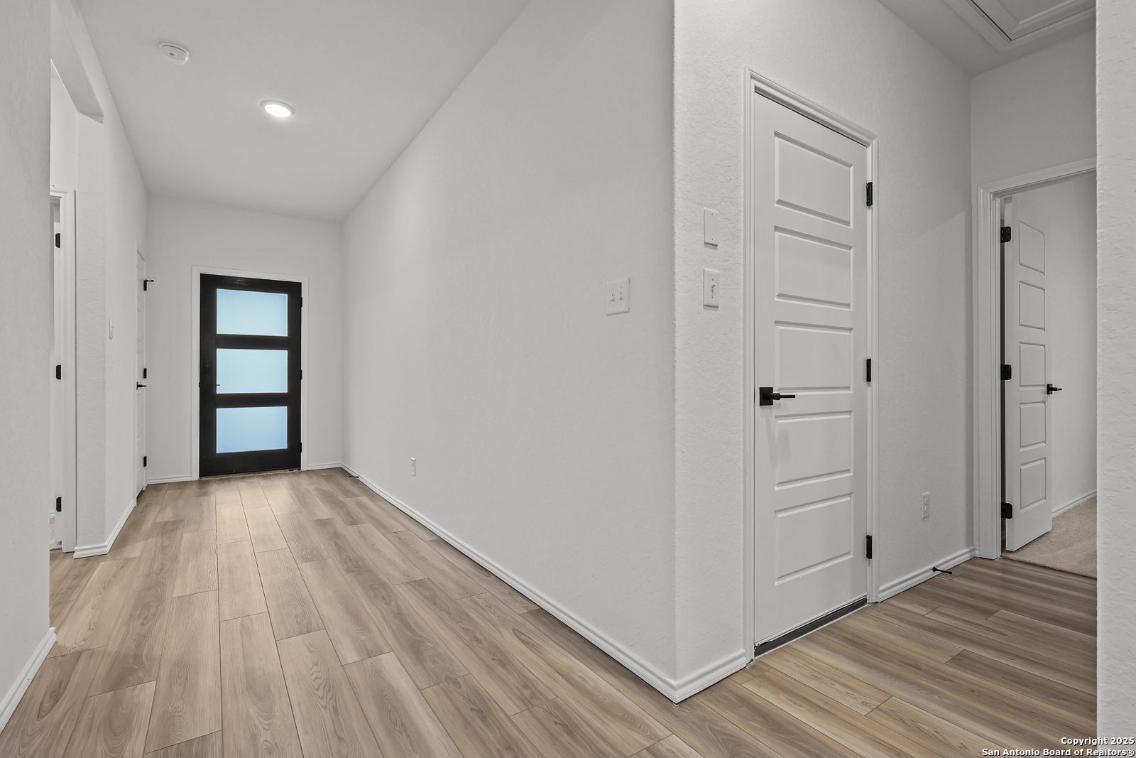 Bright hallway with white walls, light wood flooring, and paneled doors in Davidson Homes The Daphne J, Converse, Texas