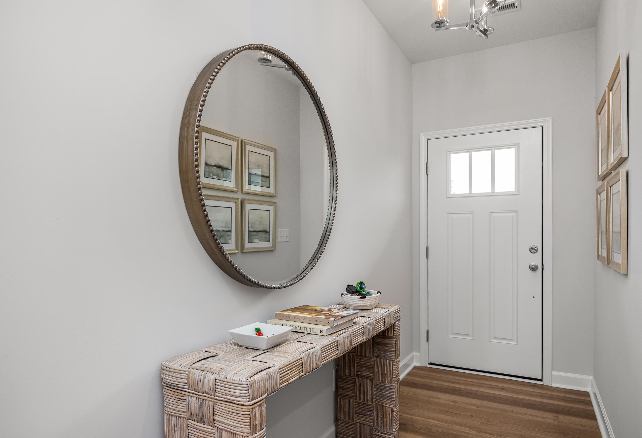 Bright foyer entryway in The Graham featuring a woven console table, round mirror, and modern door in Fuquay-Varina home.