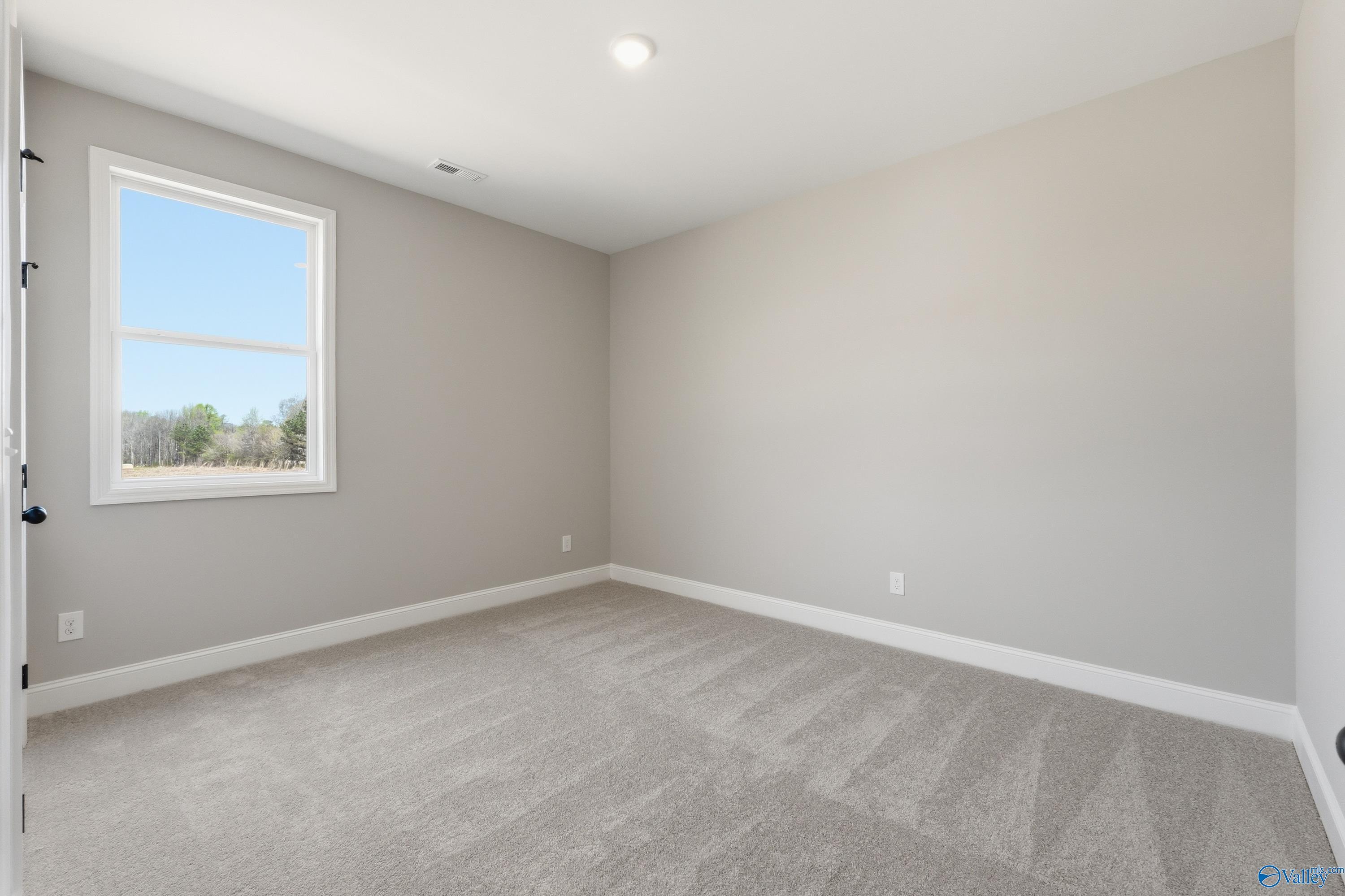 Bright empty secondary bedroom with neutral beige walls, carpet flooring, and large sunny window in Davidson Homes The Laurel K, Cullman AL