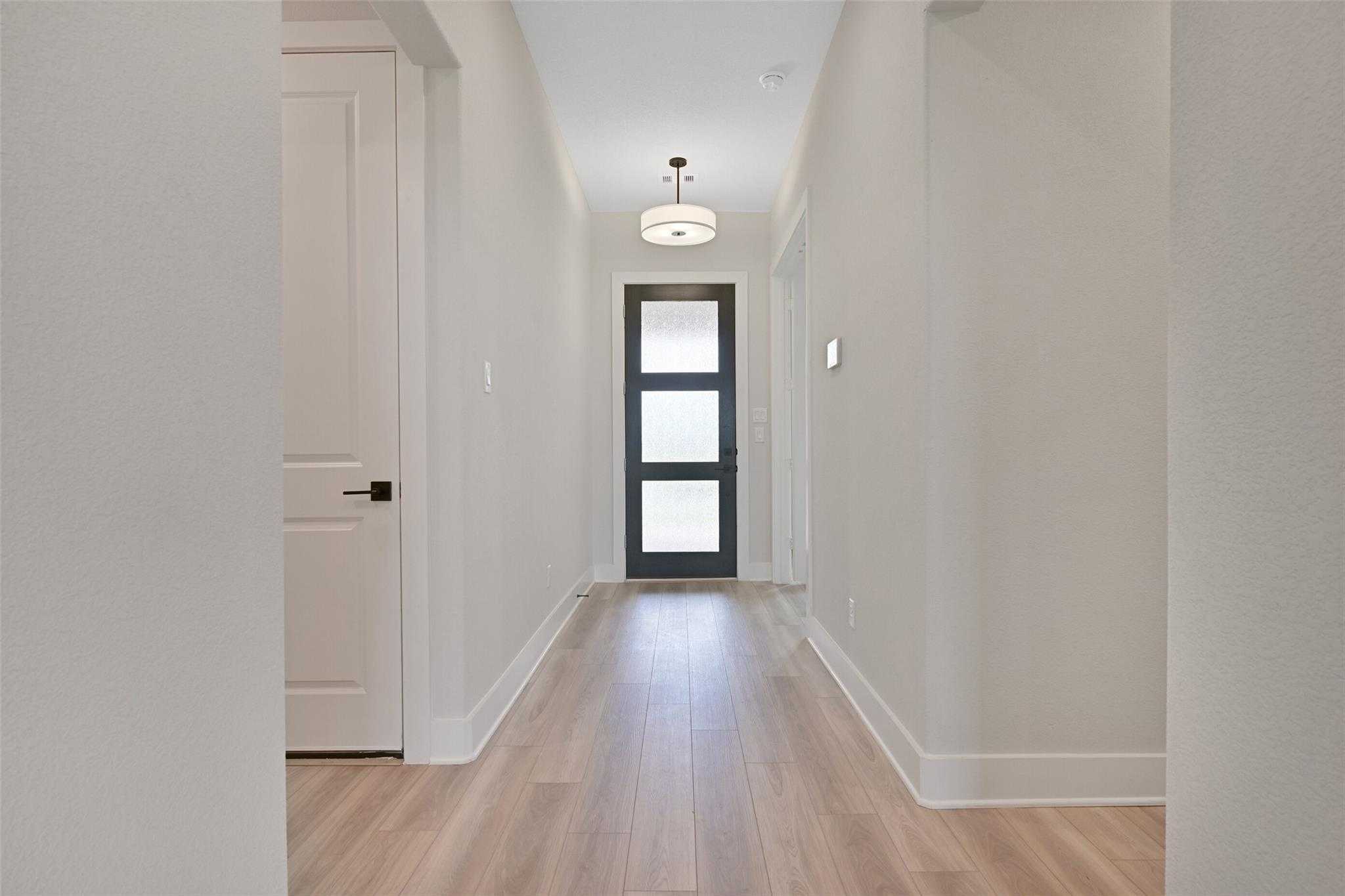 Elegant entry hallway with light oak floors, neutral walls, and modern black glass front door in Davidson Homes The Edward C, Lago Mar, Texas City