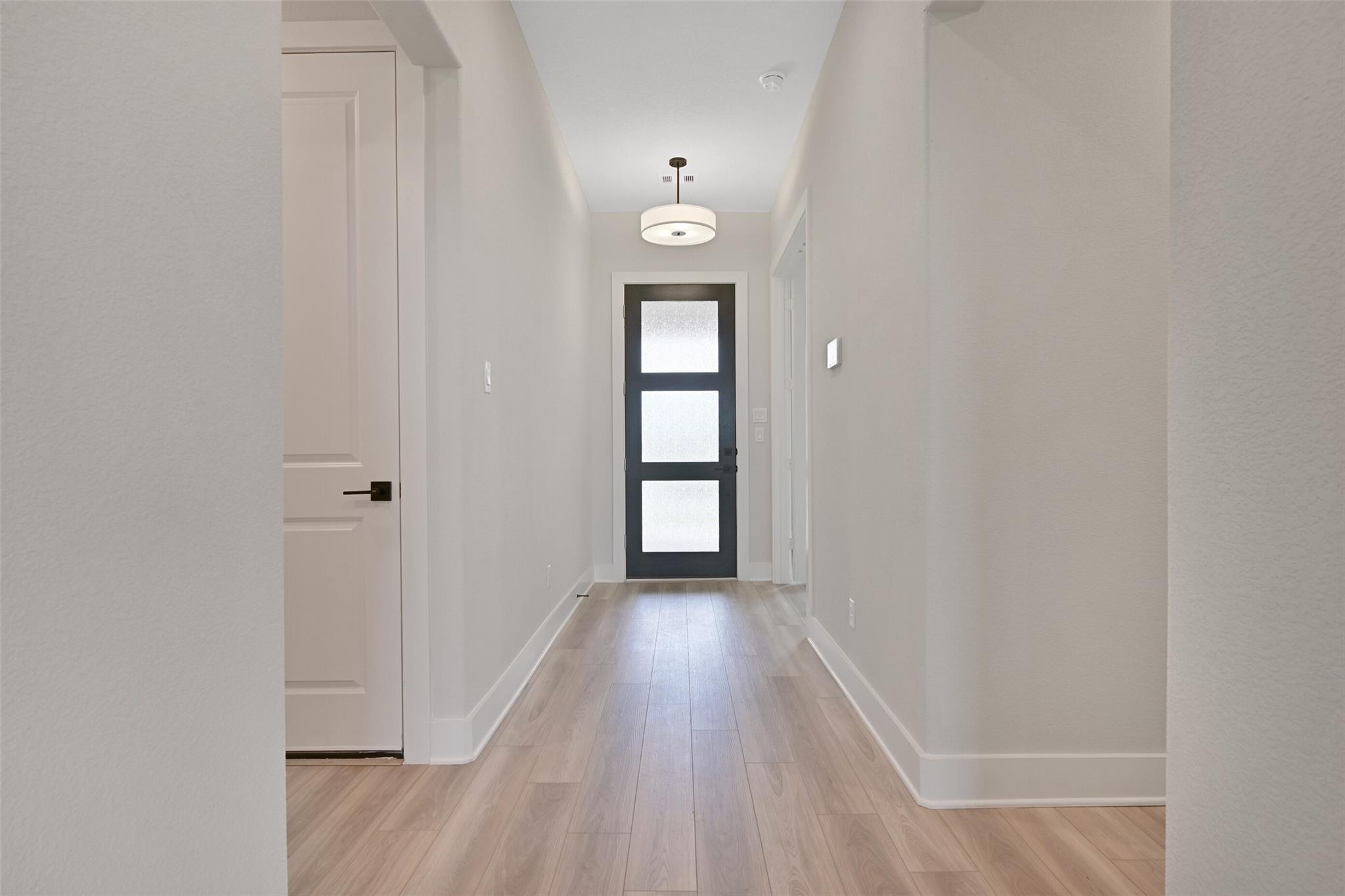 Elegant hallway with light oak floors, white walls, and black glass front door in Davidson Homes The Edward C, Lago Mar, Texas City
