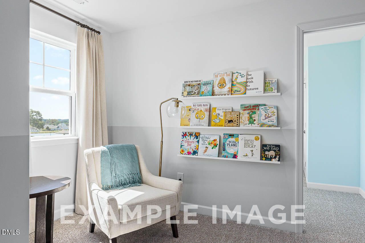 Bright reading nook with white armchair, brass lamp, and wall bookshelves in Davidson Homes The Ash C, Lillington, NC