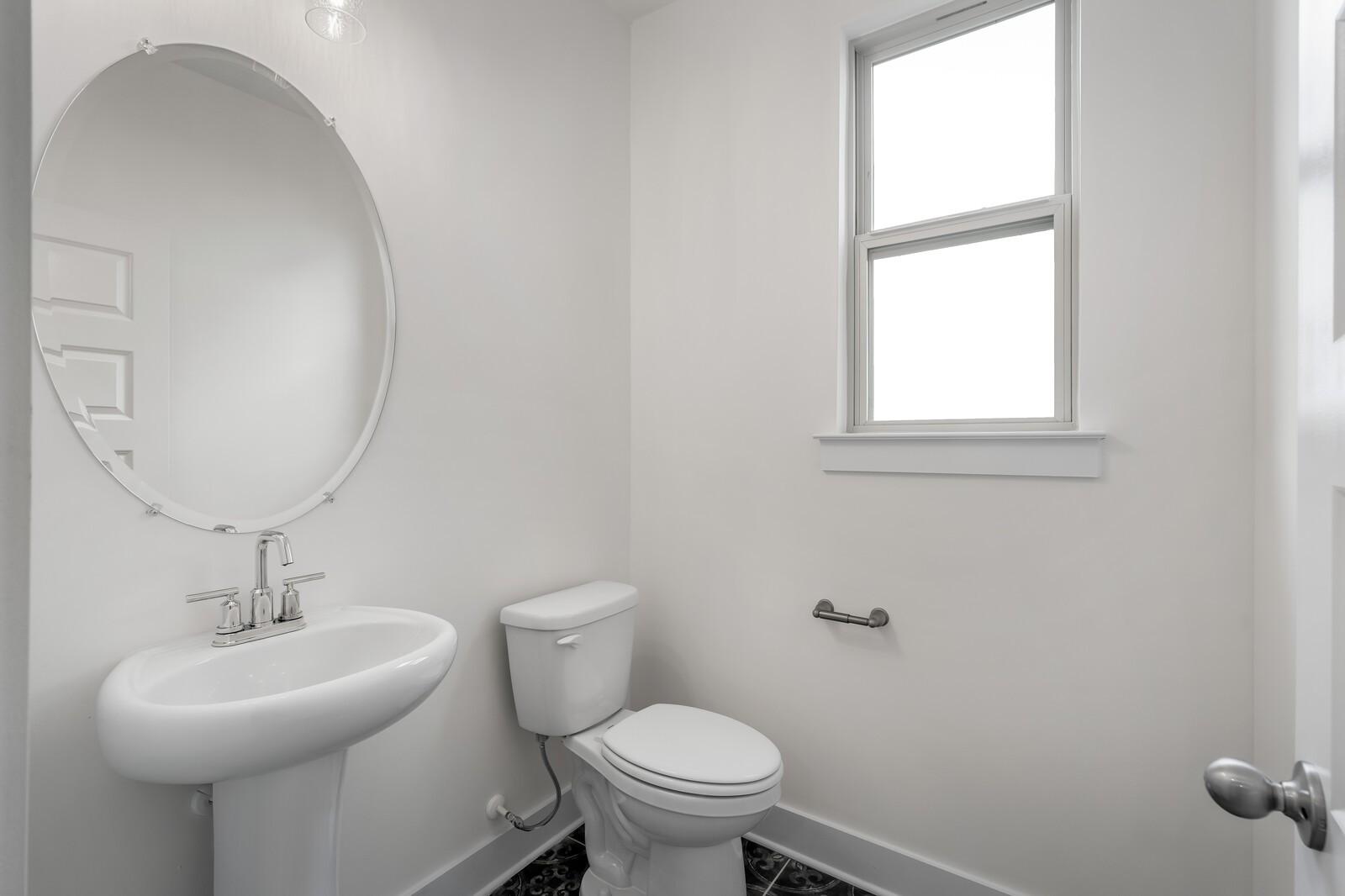 Elegant powder room featuring pedestal sink, round mirror, and window in Davidson Homes The Willow C, Gallatin, TN