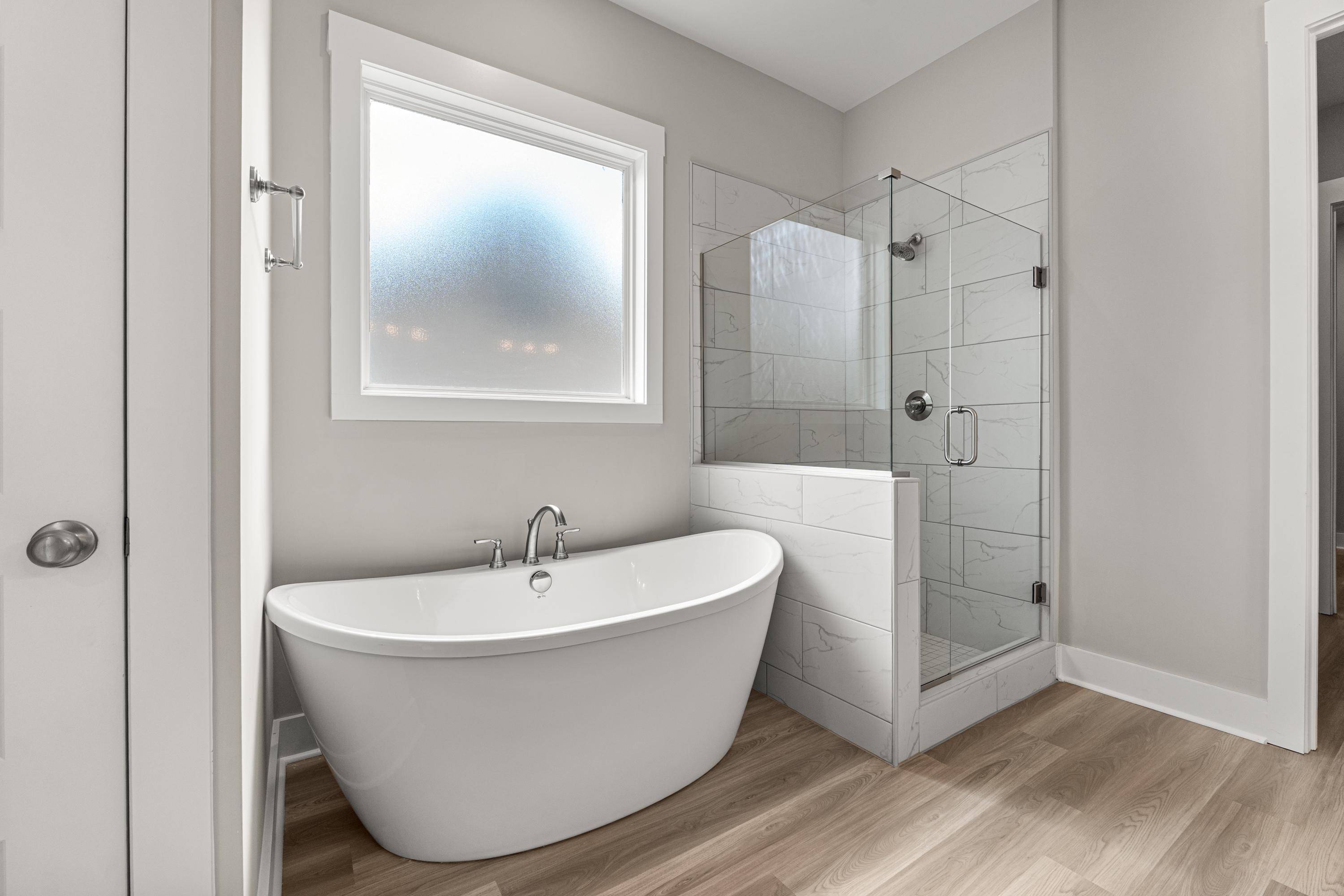 Luxury master bathroom in The Oxford C with freestanding oval tub, glass shower, and frosted window
