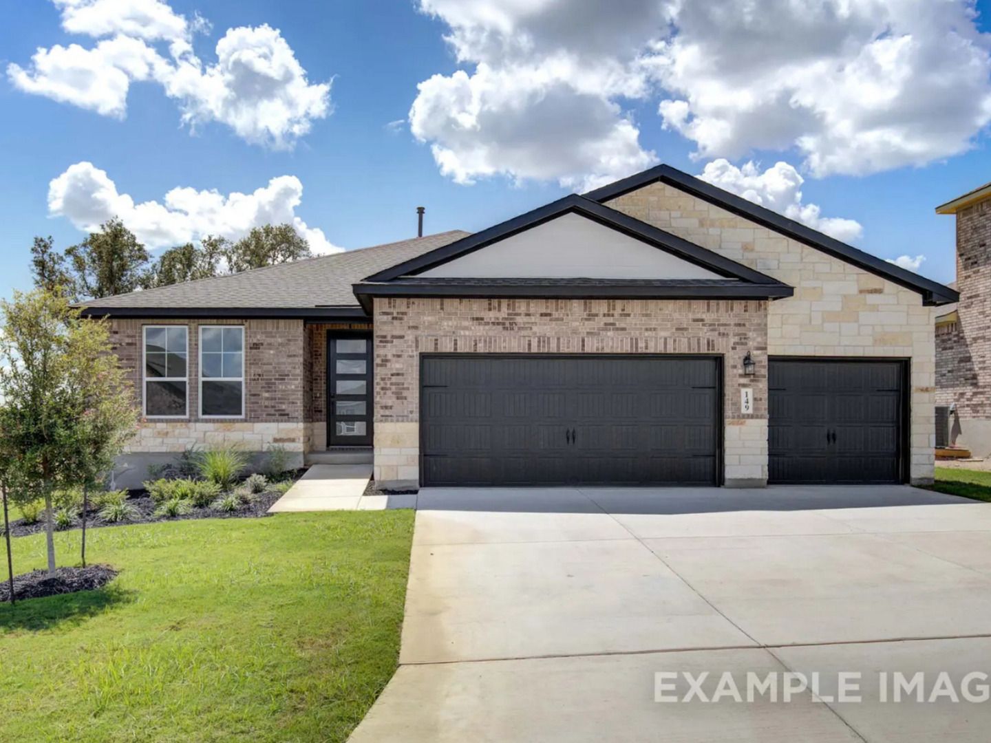 Modern 1-story brick home with black 2-car garage, landscaped yard, and blue skies in The Reserve at Potranco Oaks, Castroville, Texas