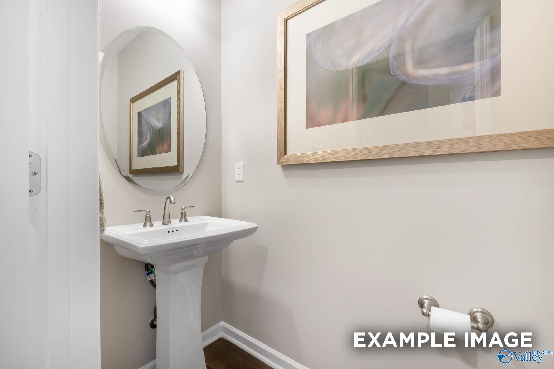 Elegant powder room with white pedestal sink, round mirror, and abstract art in Davidson Homes The Stella, Madison Alabama