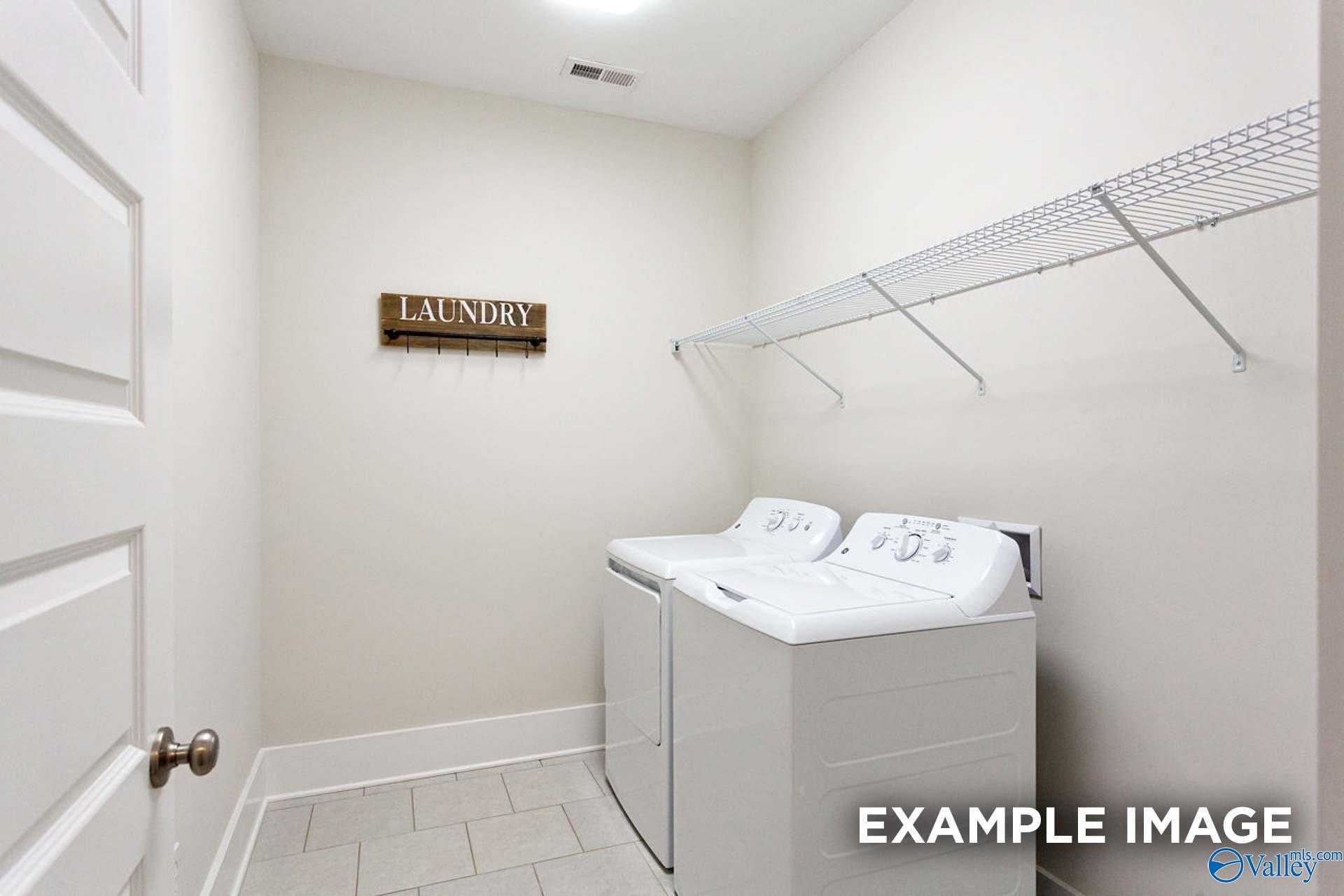 Spacious laundry room featuring white washers, dryers, wooden sign, and wire shelving in Davidson Homes The Finleigh, Meridianville, Alabama