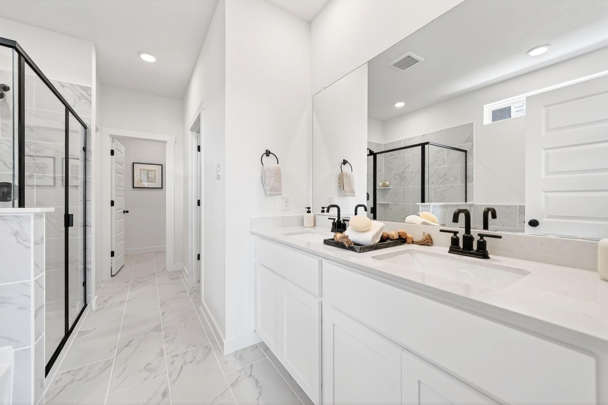 Modern bathroom with white double vanity, marble-look tile, and black fixtures at The Parks at Foster Crossing in Anna, TX.