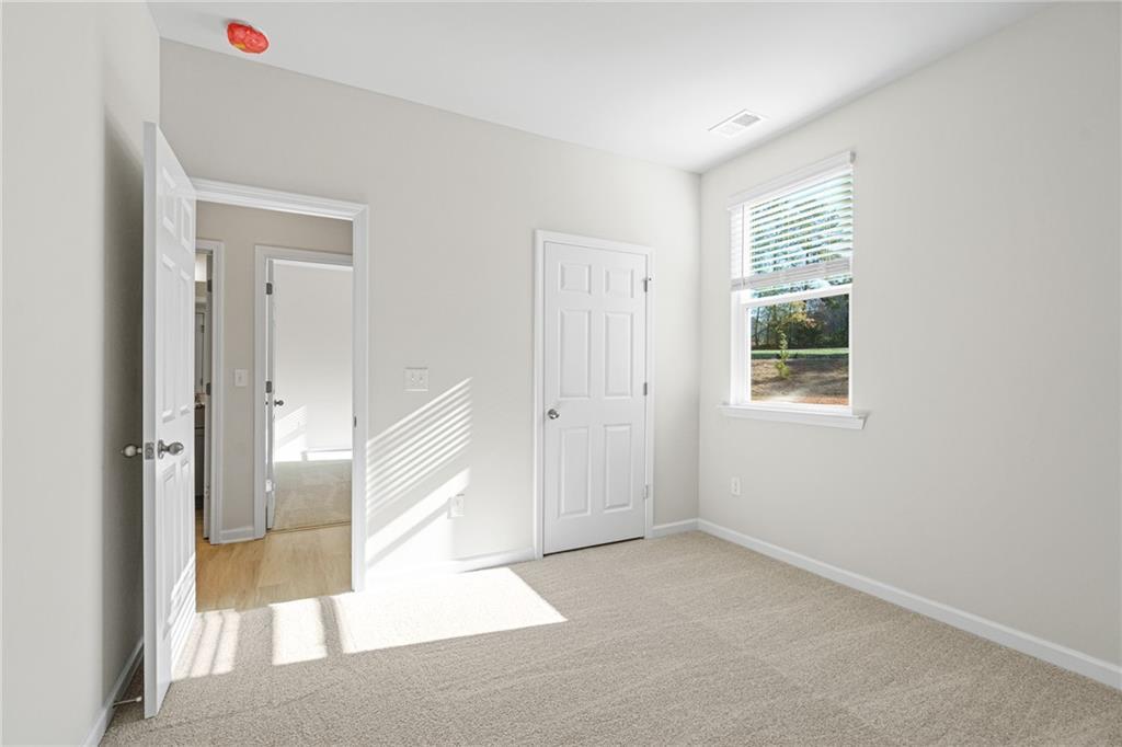 Bright bedroom with neutral carpet and window in The Glenwood A floor plan at Wehunt Meadows, Hoschton, Georgia.