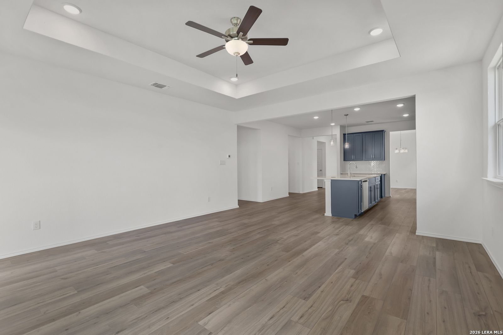 Open-concept living area with tray ceiling, ceiling fan, and luxury vinyl plank floors opening to navy island kitchen in The Glenwood E, Elmendorf TX