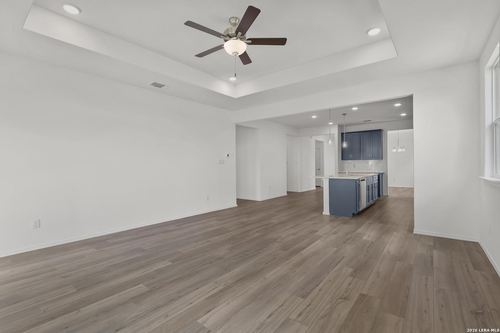 Open-concept living area with tray ceiling, ceiling fan, and luxury vinyl plank floors opening to navy island kitchen in The Glenwood E, Elmendorf TX