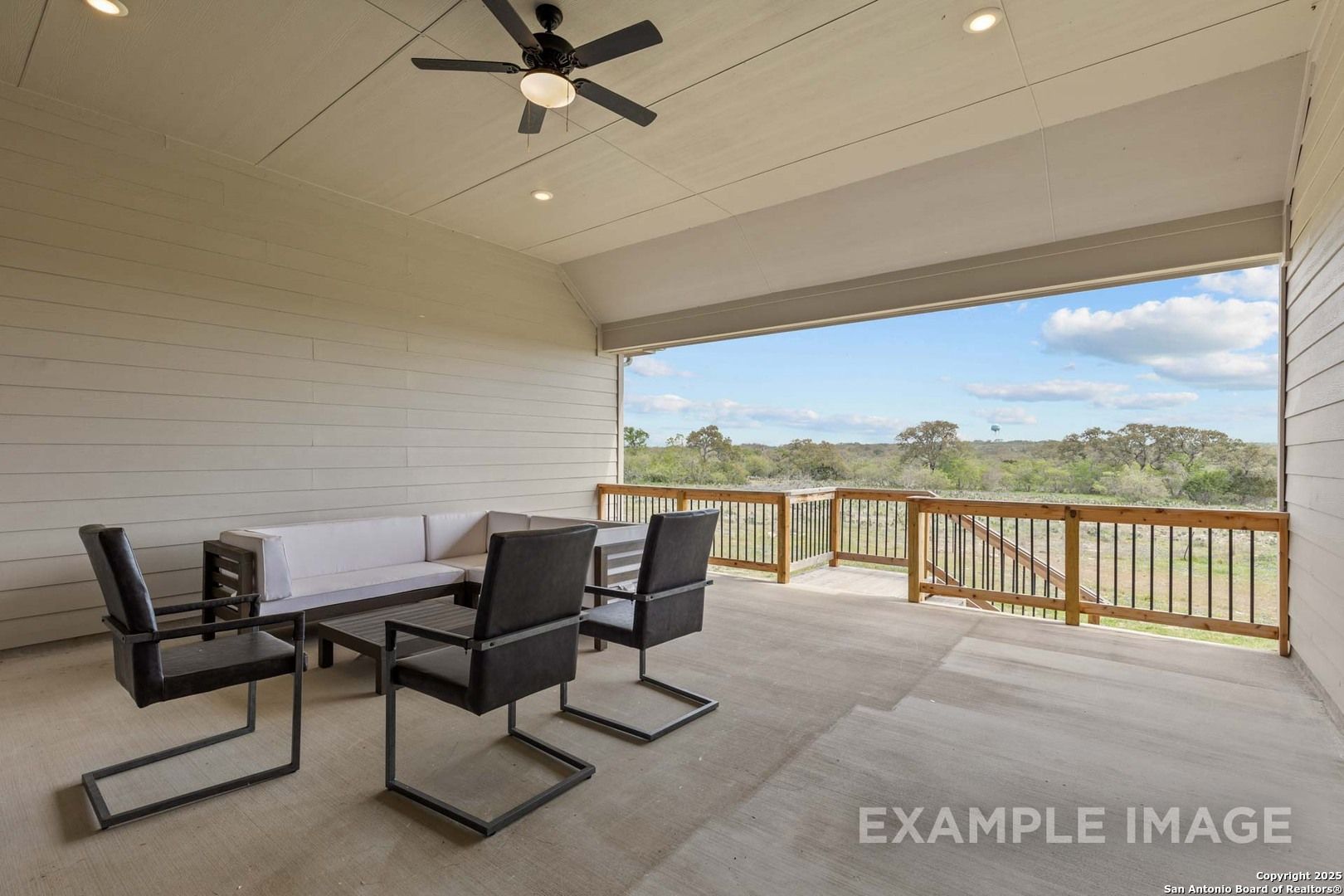 Covered patio with ceiling fan, modern sectional sofa, and chairs overlooking wooded yard in Davidson Homes The Summerlin B, Castroville, Texas