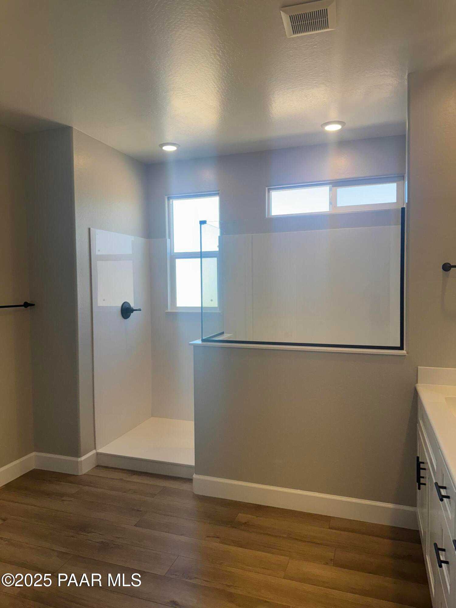 Modern master bathroom with frameless glass shower enclosure, white tile, and wood flooring in Evermore Homes The Summit B, Prescott Valley, AZ