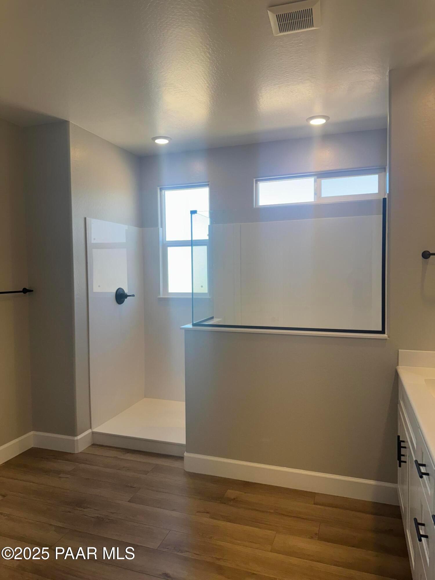 Modern master bathroom with frameless glass shower enclosure, white tile, and wood flooring in Evermore Homes The Summit B, Prescott Valley, AZ
