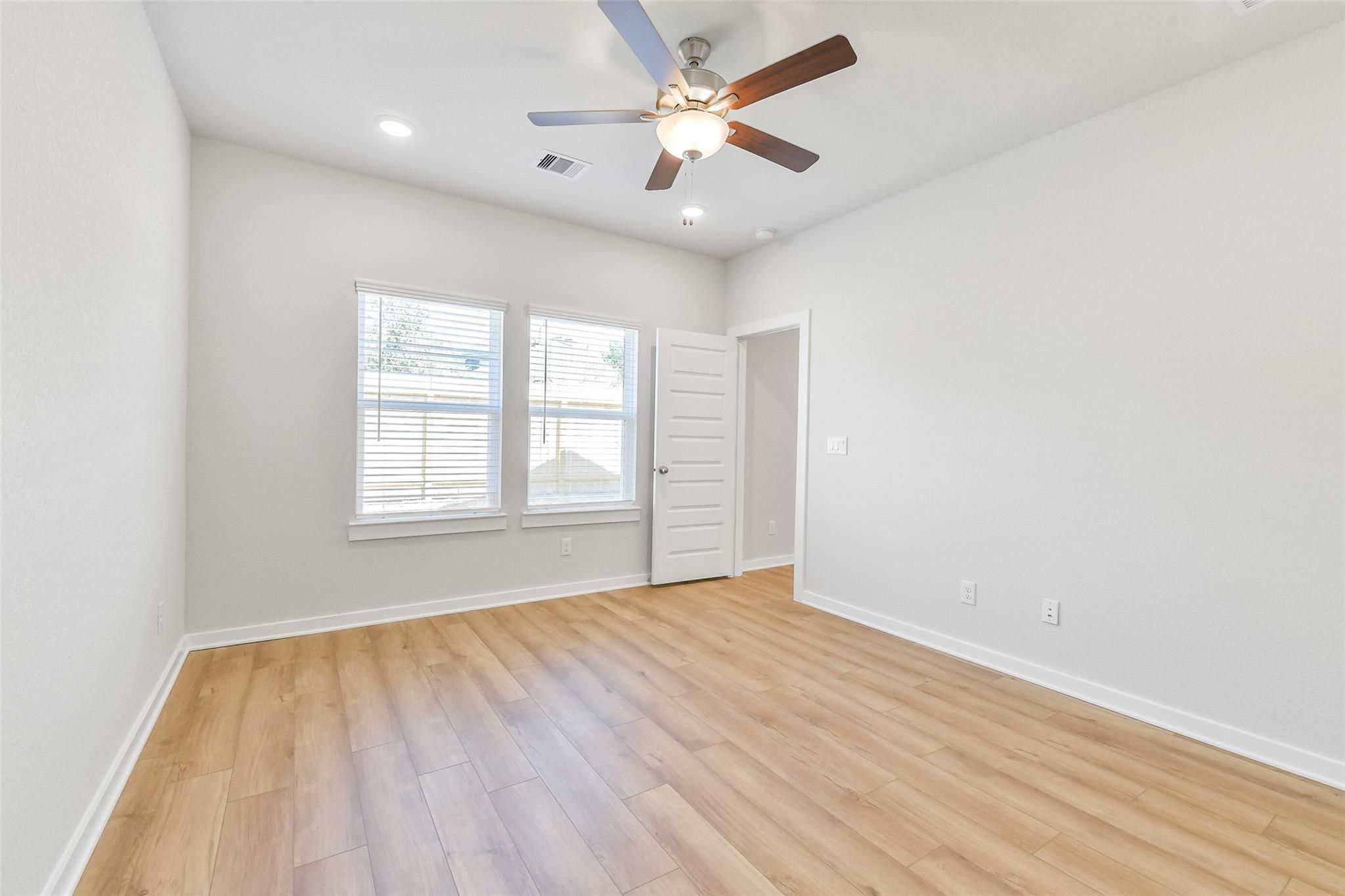 Bright secondary bedroom with ceiling fan, hardwood floors, and large windows in Davidson Homes The Blanco E, Magnolia, Texas
