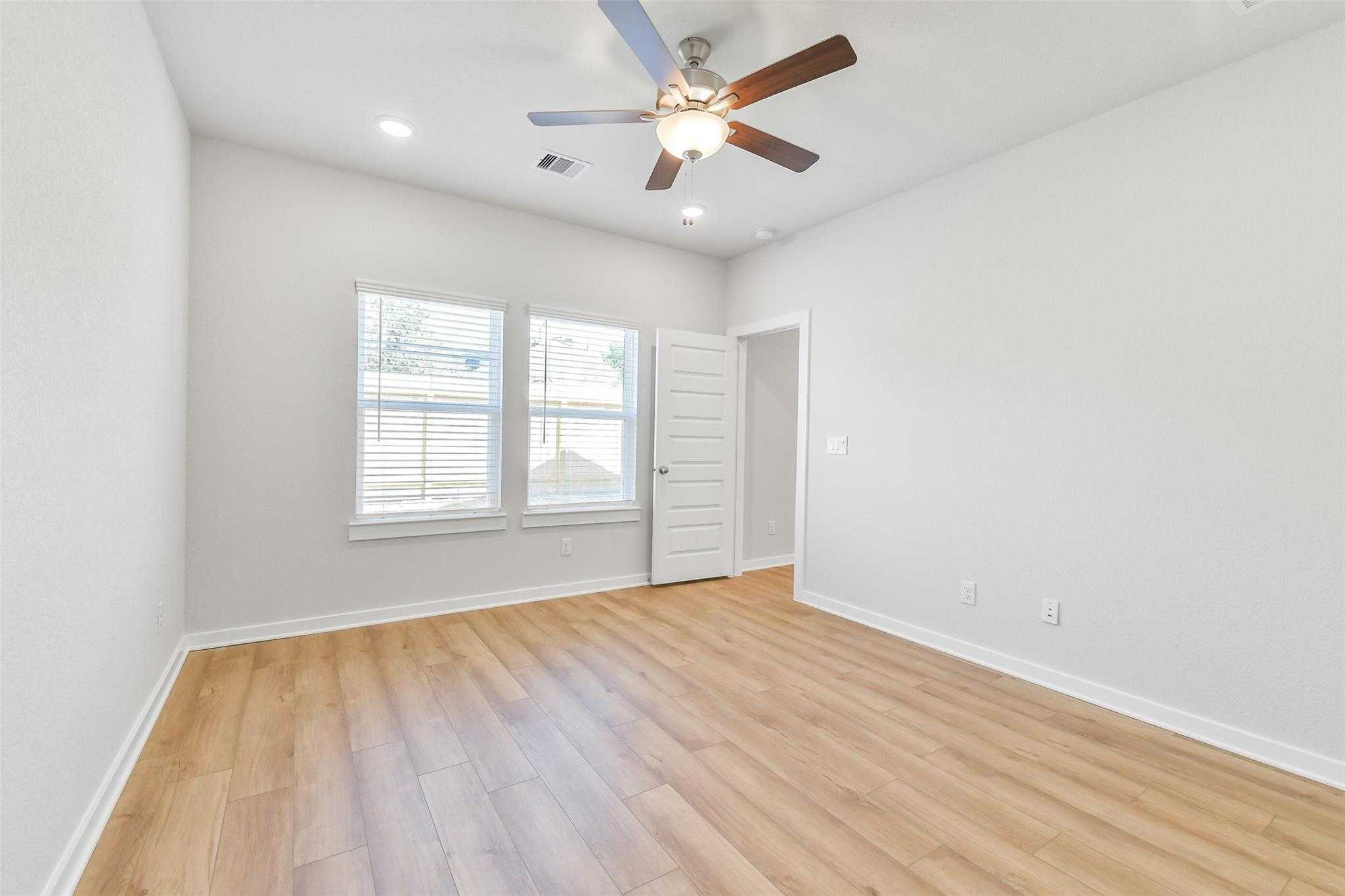 Bright secondary bedroom with ceiling fan, hardwood floors, and large windows in Davidson Homes The Blanco E, Magnolia, Texas