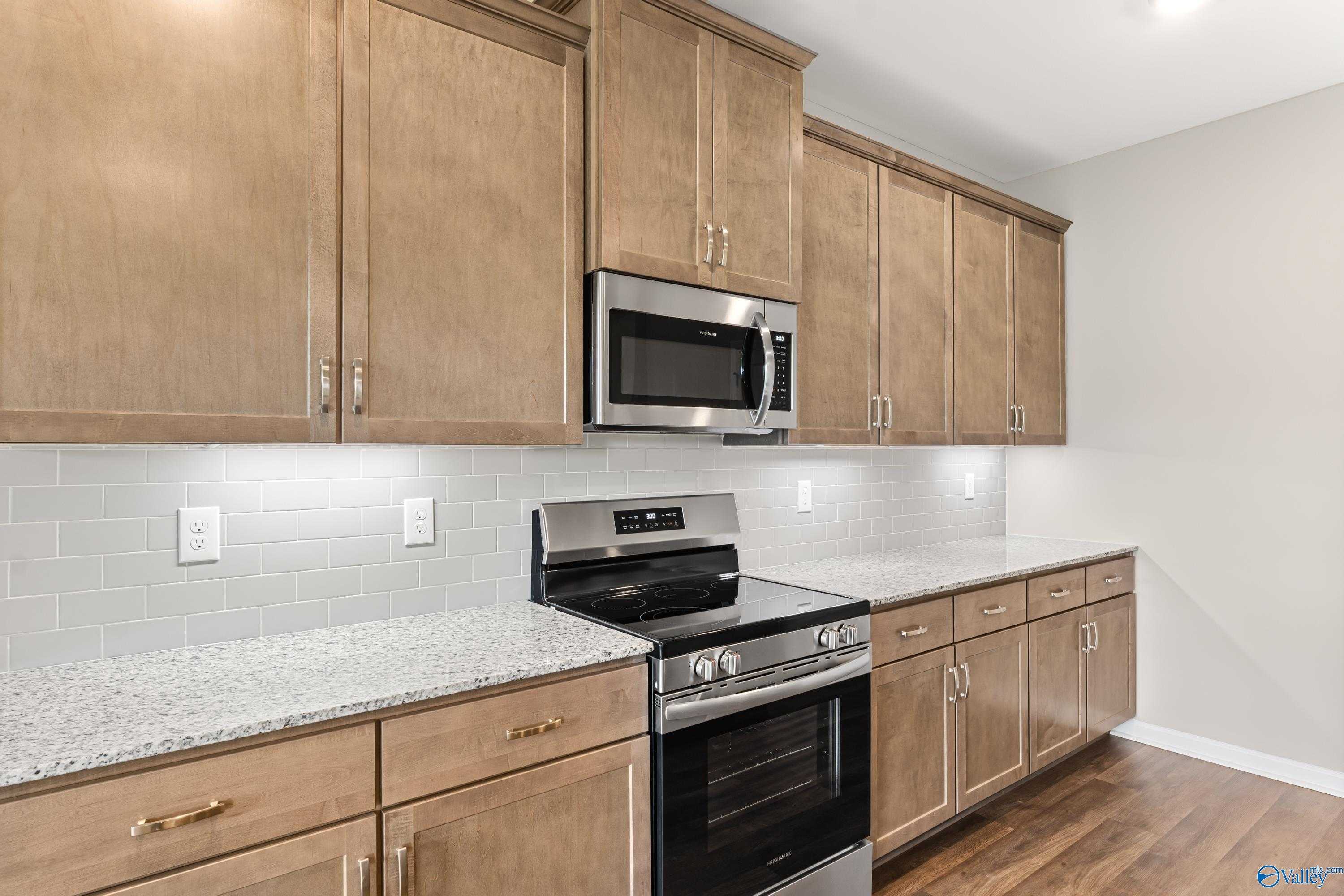 Modern kitchen featuring shaker-style beige cabinets, granite countertops, stainless steel range, and subway tile backsplash in Davidson Homes The Haven, Huntsville AL