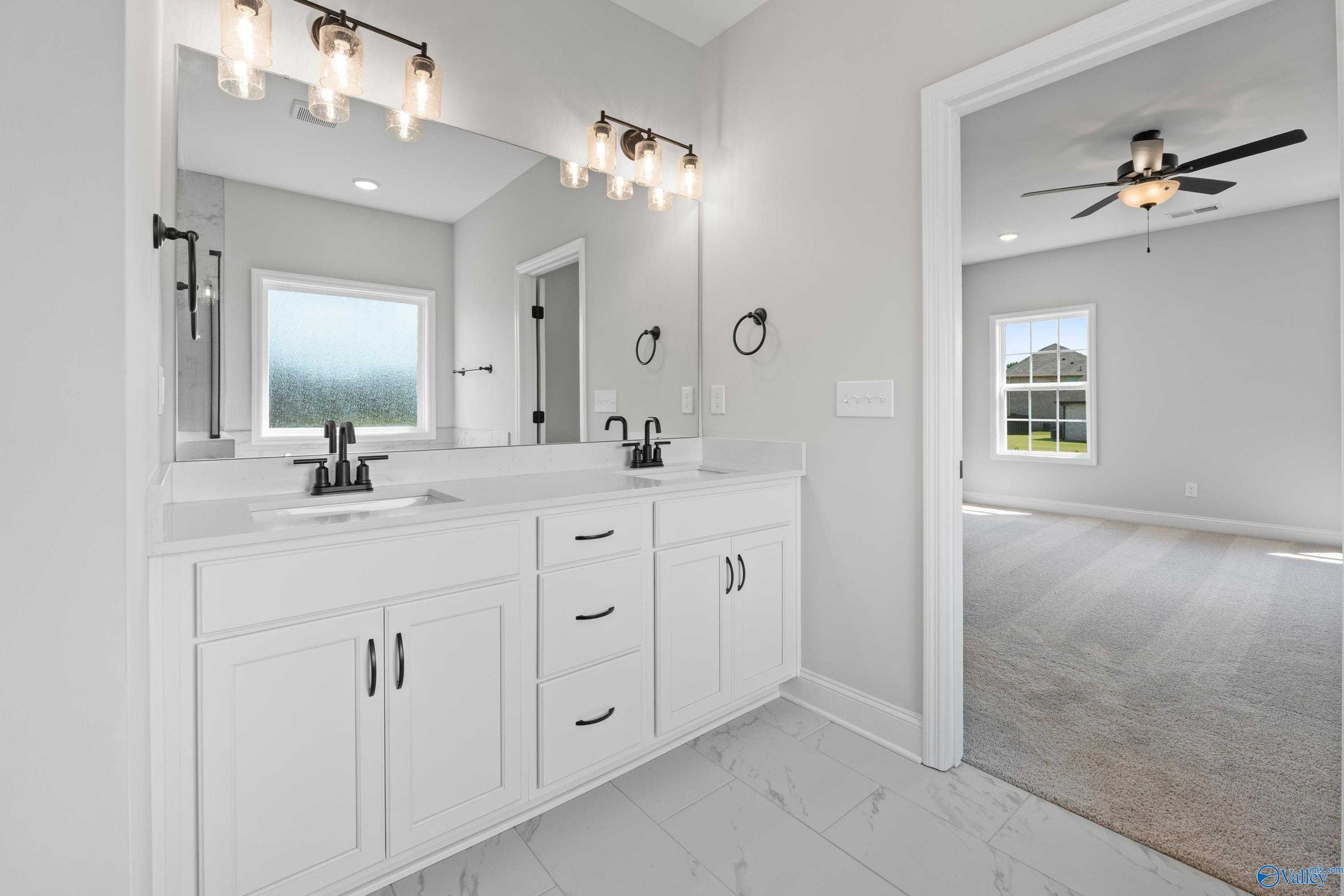Modern master bathroom featuring double white vanity, lighted mirrors, and rain-streaked window in Davidson Homes The Rockford, Toney, Alabama