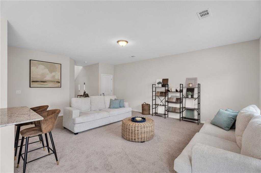 Bright family room with white sofas, teal pillows, woven ottoman, and bar seating in Davidson Homes The Bartlett, Phenix City