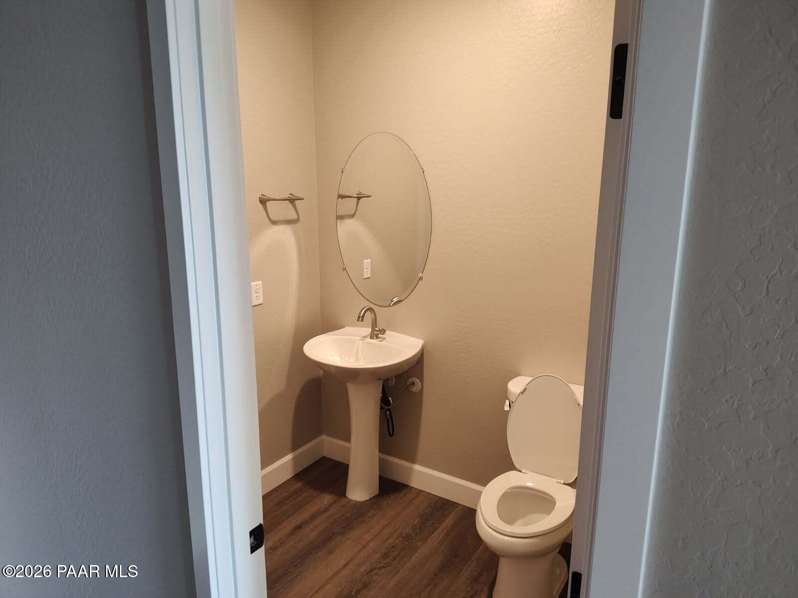Elegant half bath with pedestal sink, round frameless mirror, and white toilet in Davidson Homes The Harmony C, Prescott Valley, AZ