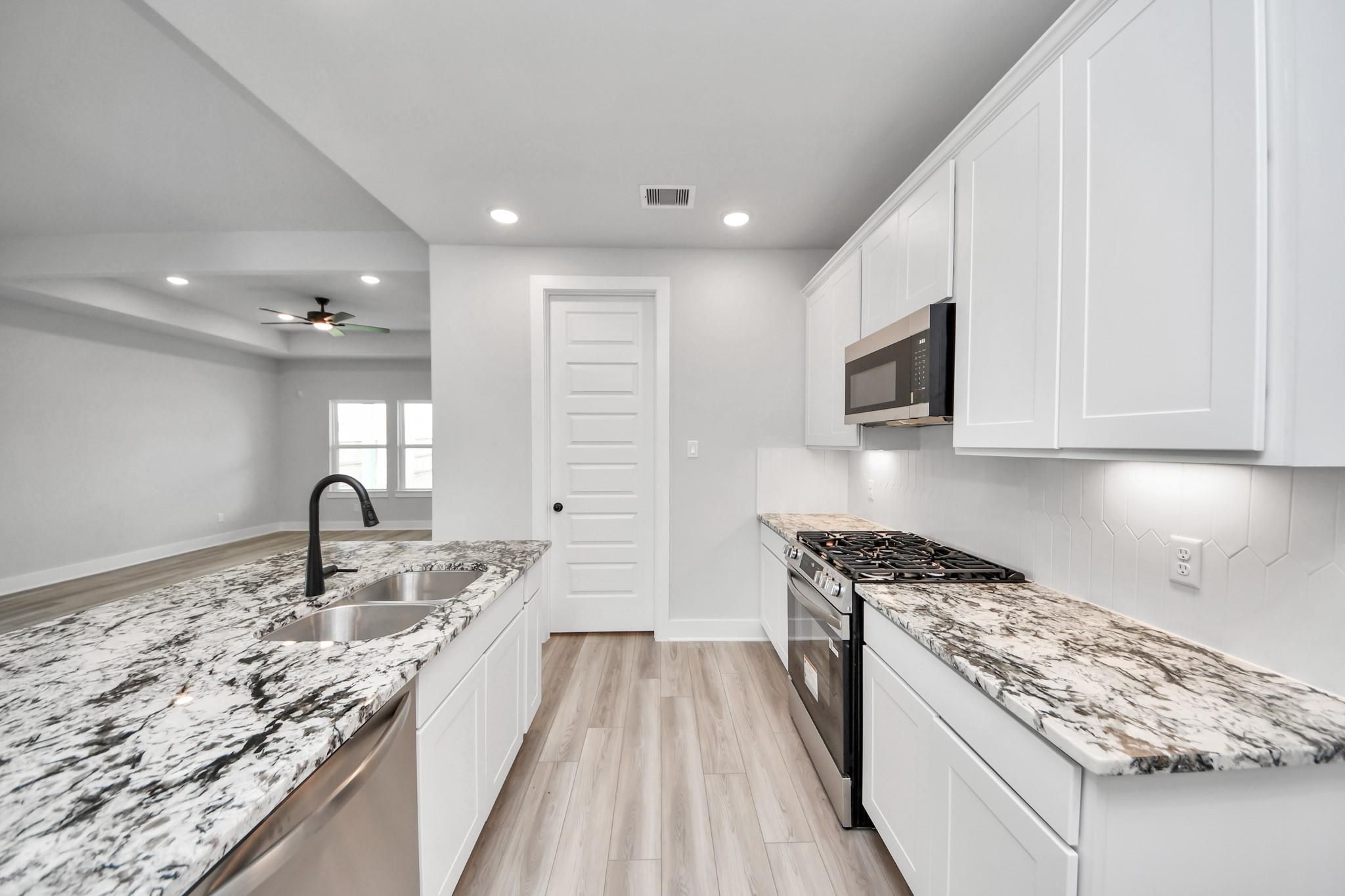 Modern kitchen with granite countertops, white cabinetry, and stainless appliances in The Laguna C home, Sunterra, Katy, TX.