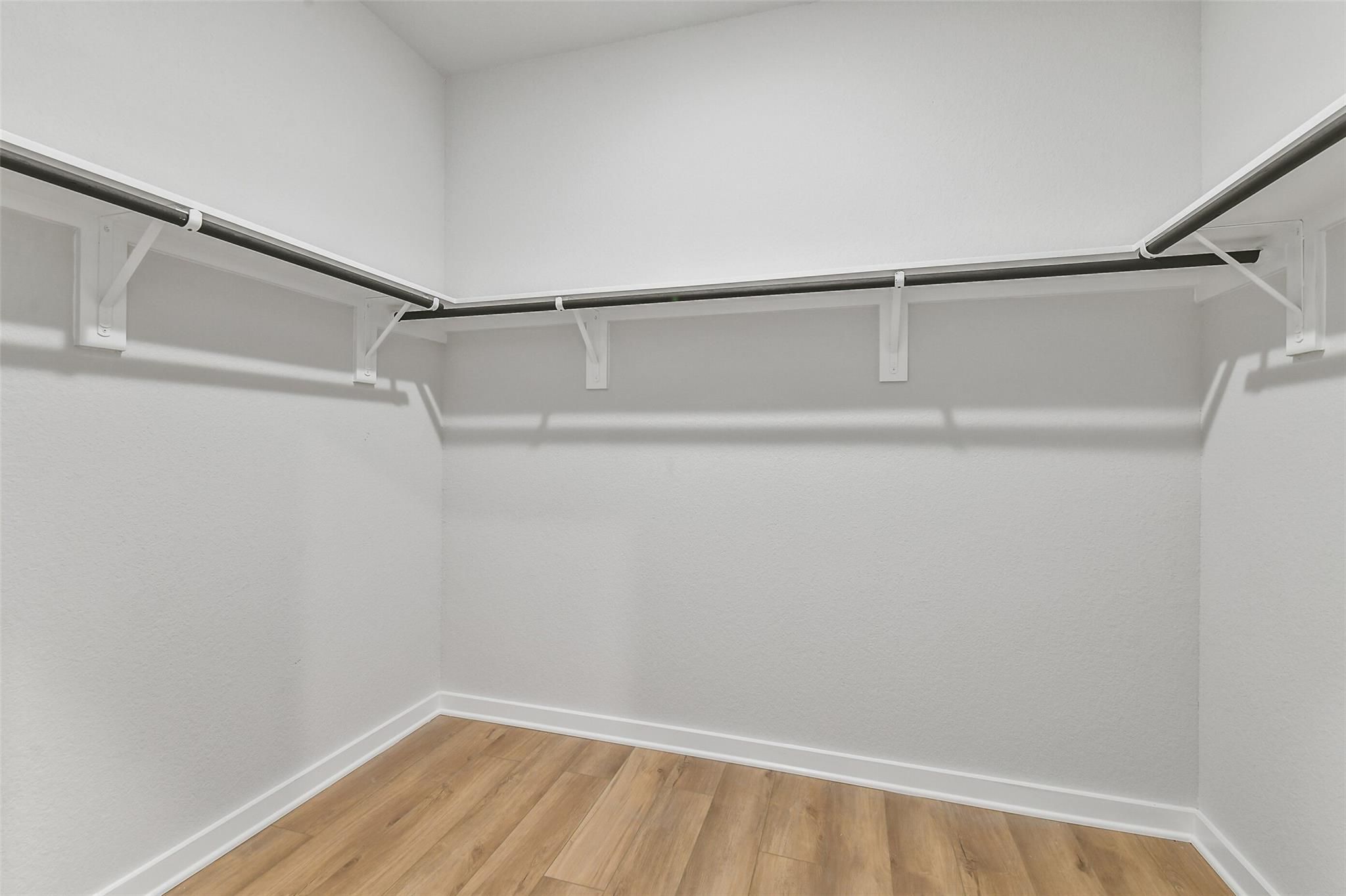 Walk-in closet with white hanging rods, brackets, and light oak flooring in Davidson Homes The Blanco E, Magnolia, Texas