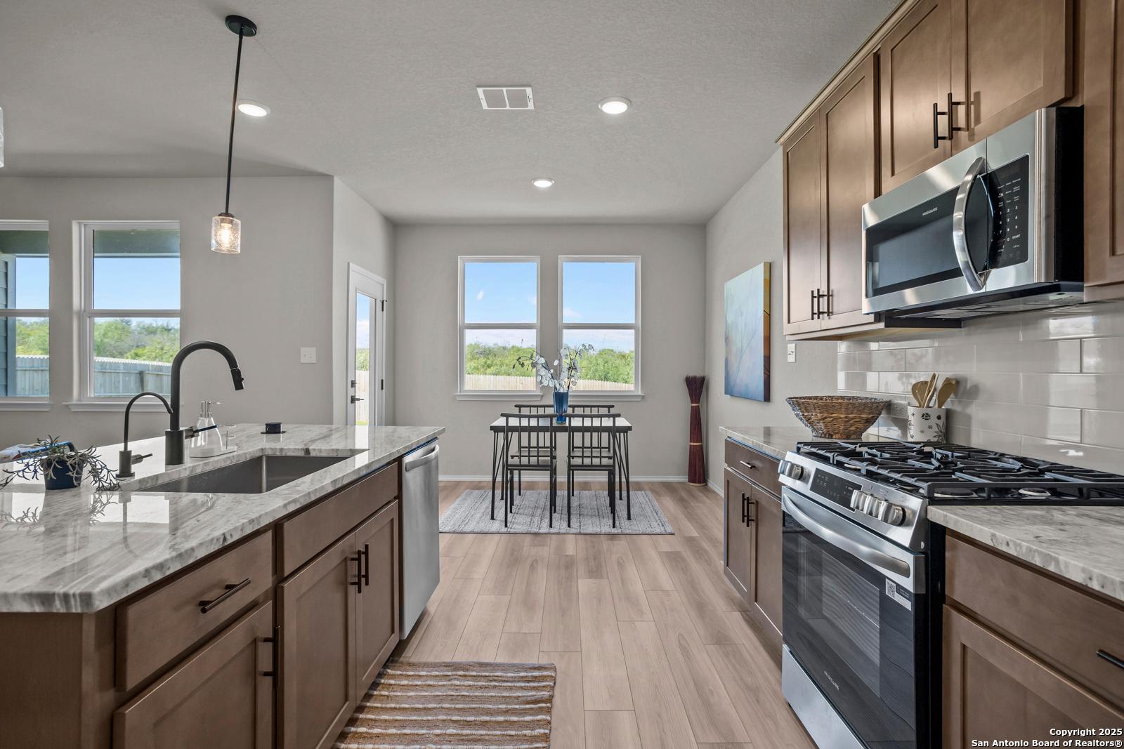 Open-concept kitchen with stainless steel appliances, white quartz countertops, and dining nook in The Asheville H by Davidson Homes, Converse, Texas