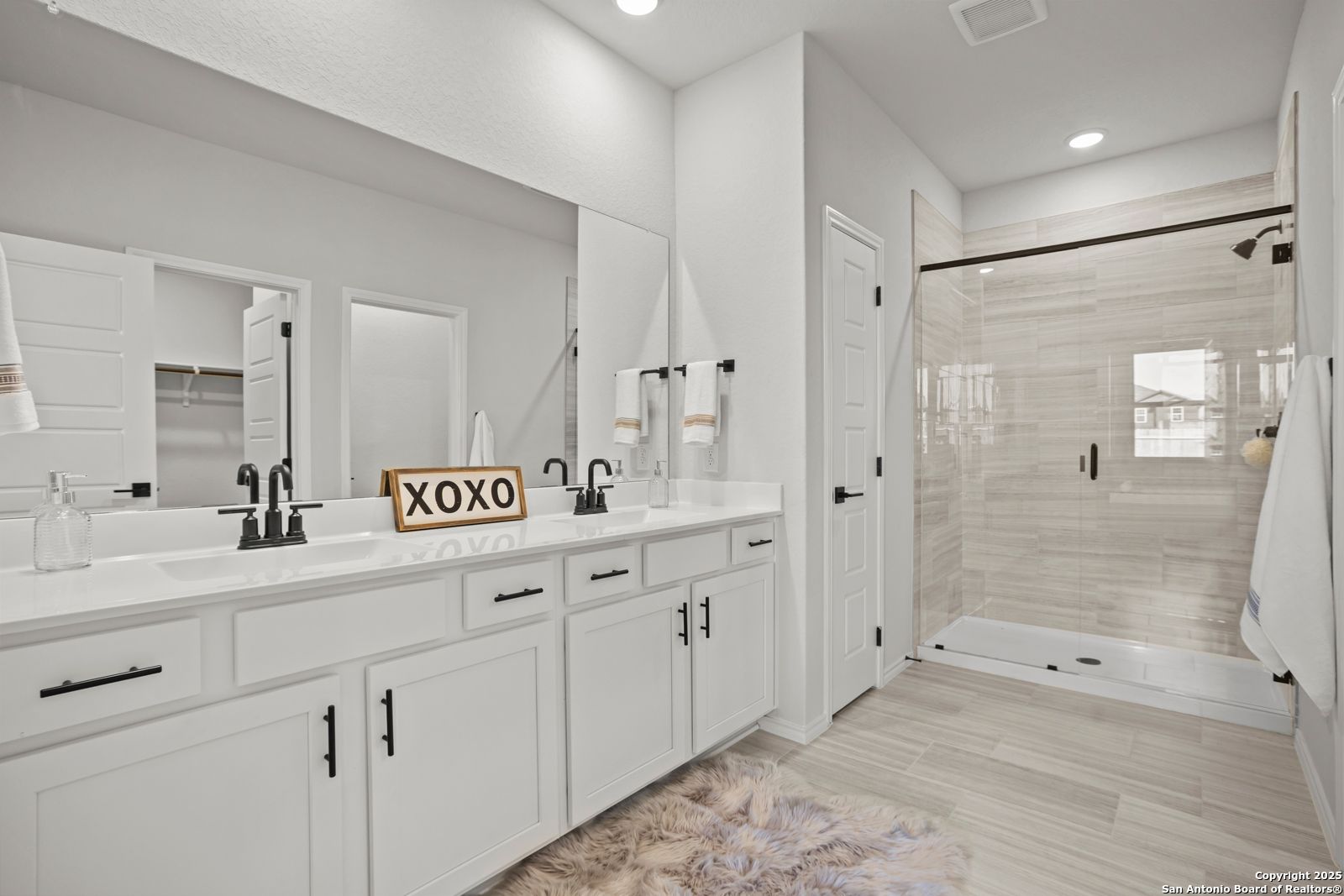 Modern master bathroom with double vanity sinks, frameless glass shower, white shaker cabinets in Davidson Homes The Douglas C, Seguin, Texas