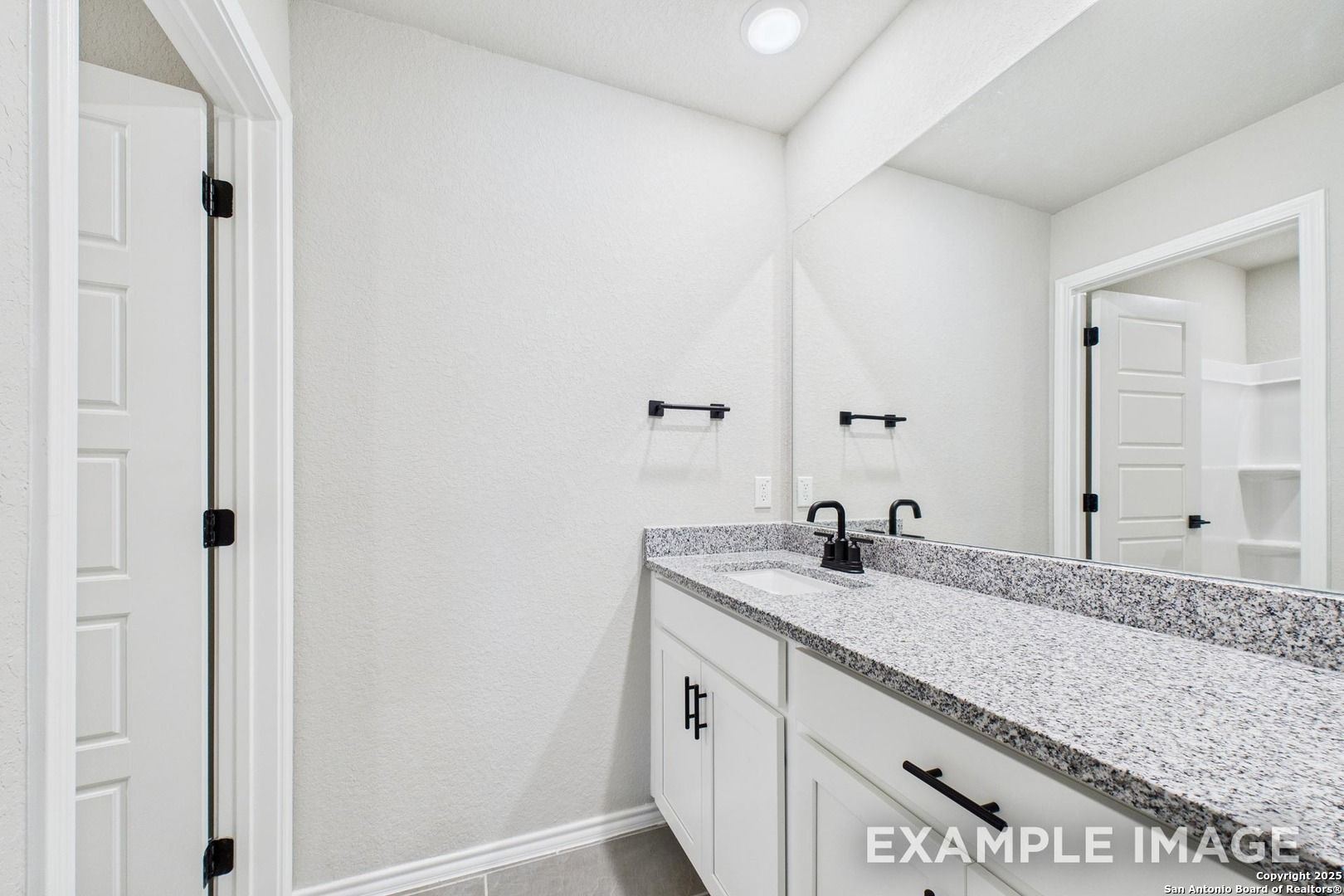 Granite vanity with white cabinets, single sink, and large mirror in master bathroom of Davidson Homes The Charlotte A, San Antonio