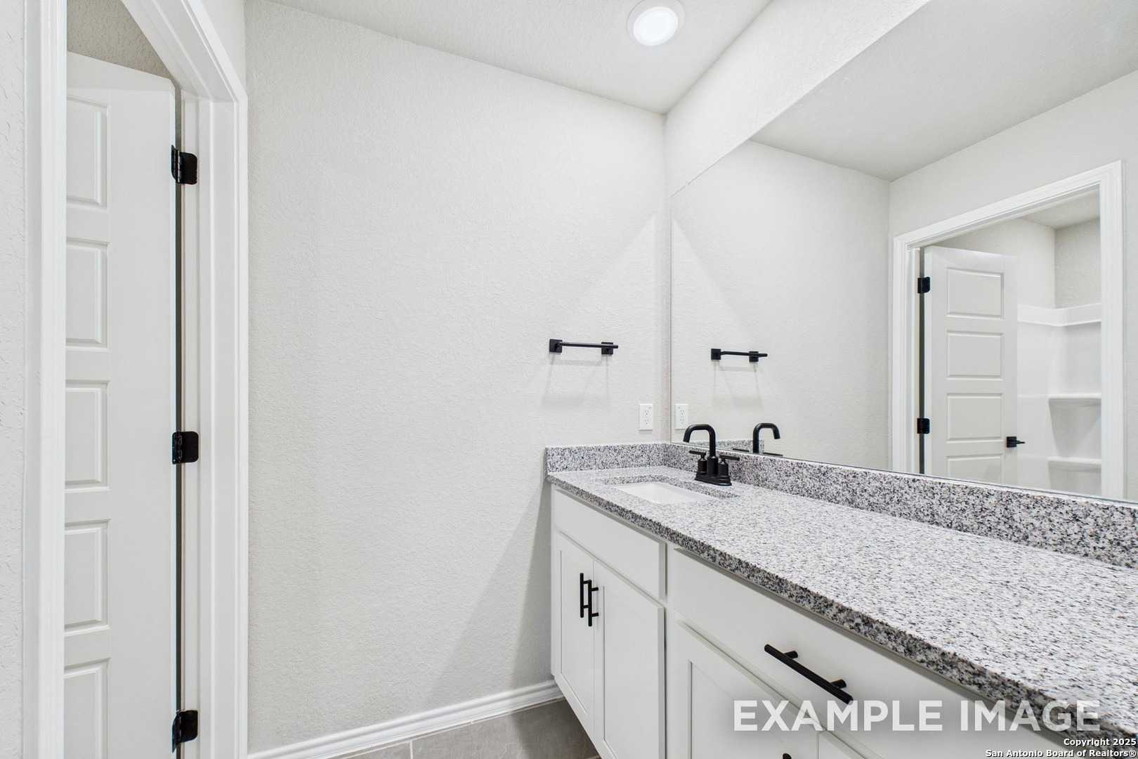Granite vanity with white cabinets, single sink, and large mirror in master bathroom of Davidson Homes The Charlotte A, San Antonio