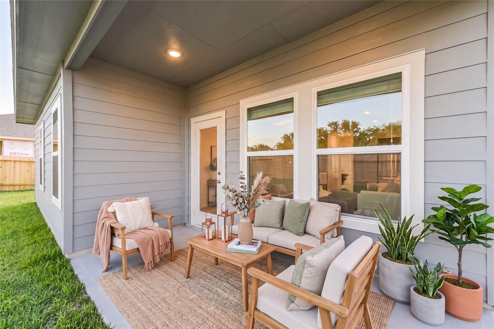 Covered back patio with teak sofa, armchairs, coffee table, potted plants, and lanterns in Davidson Homes The Costa C, Dayton, Texas