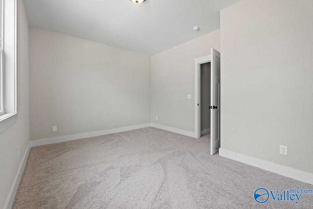 Bright empty secondary bedroom with beige walls, carpeted floor, and large window in Evermore Homes The Oxford, Owens Cross Roads, Alabama