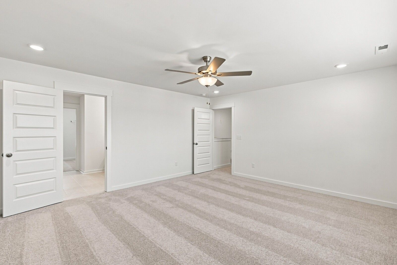 Spacious carpeted bedroom with ceiling fan and white doors in Davidson Homes The Willow C plan at Woods Crossing, Gallatin, TN