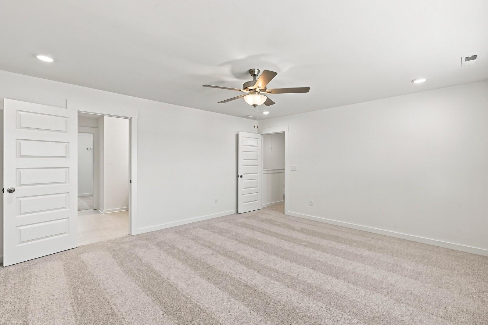 Spacious carpeted bedroom with ceiling fan and white doors in Davidson Homes The Willow C plan at Woods Crossing, Gallatin, TN